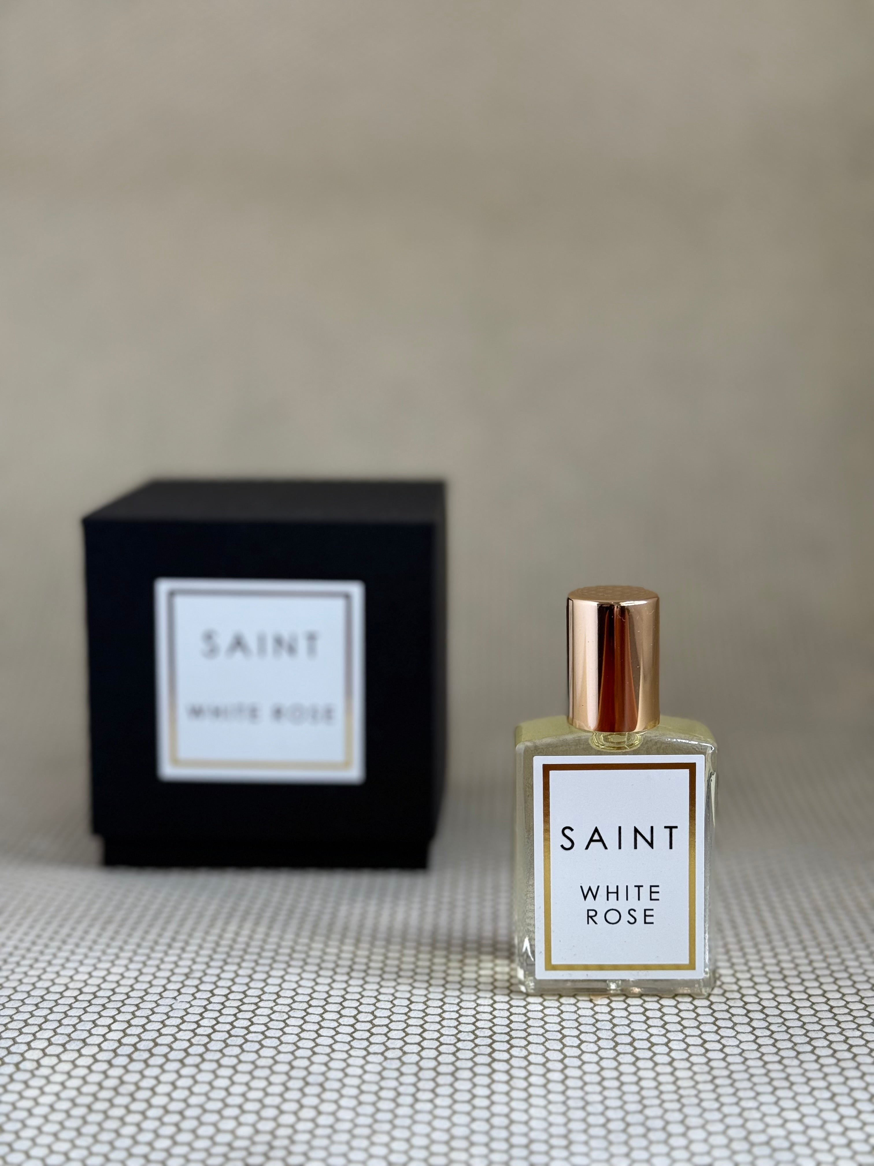 Perfume bottle and packaging labeled 'Saint White Rose' on a textured surface with a neutral background.