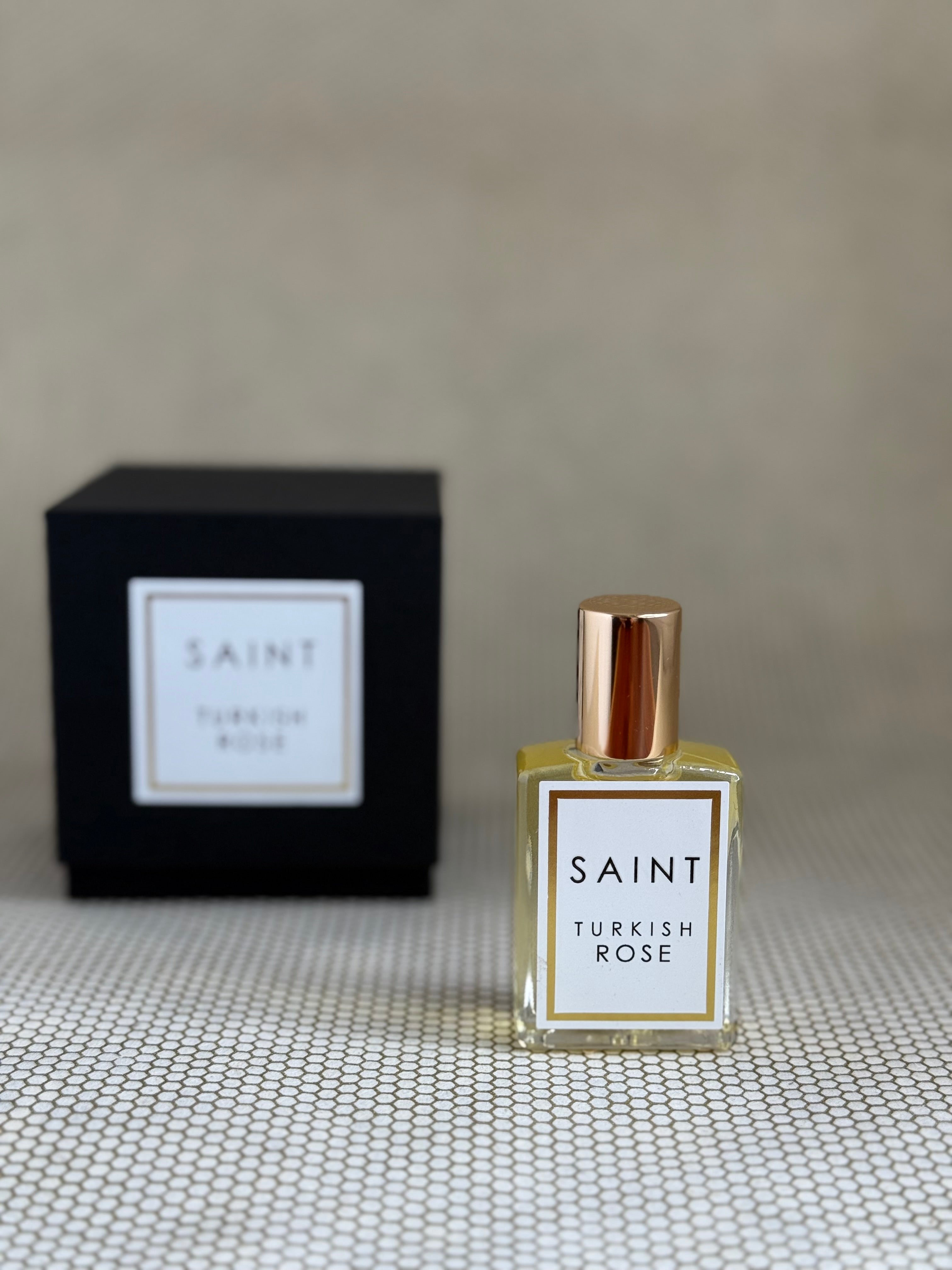 Perfume bottle labeled 'Saint Turkish Rose' with a black box in the background on a textured surface.