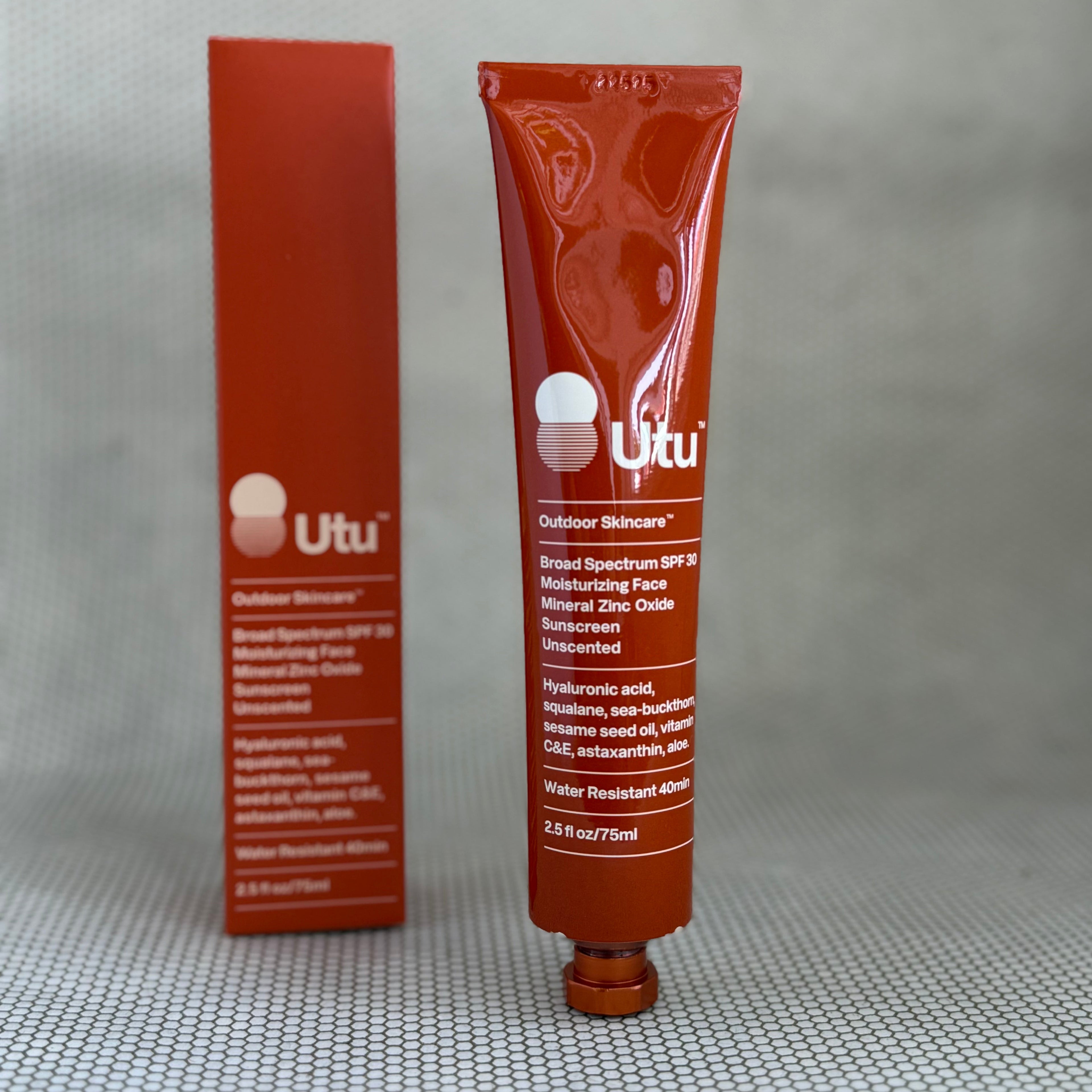 Orange tube of Utu outdoor skincare and orange packaging box on a gray background