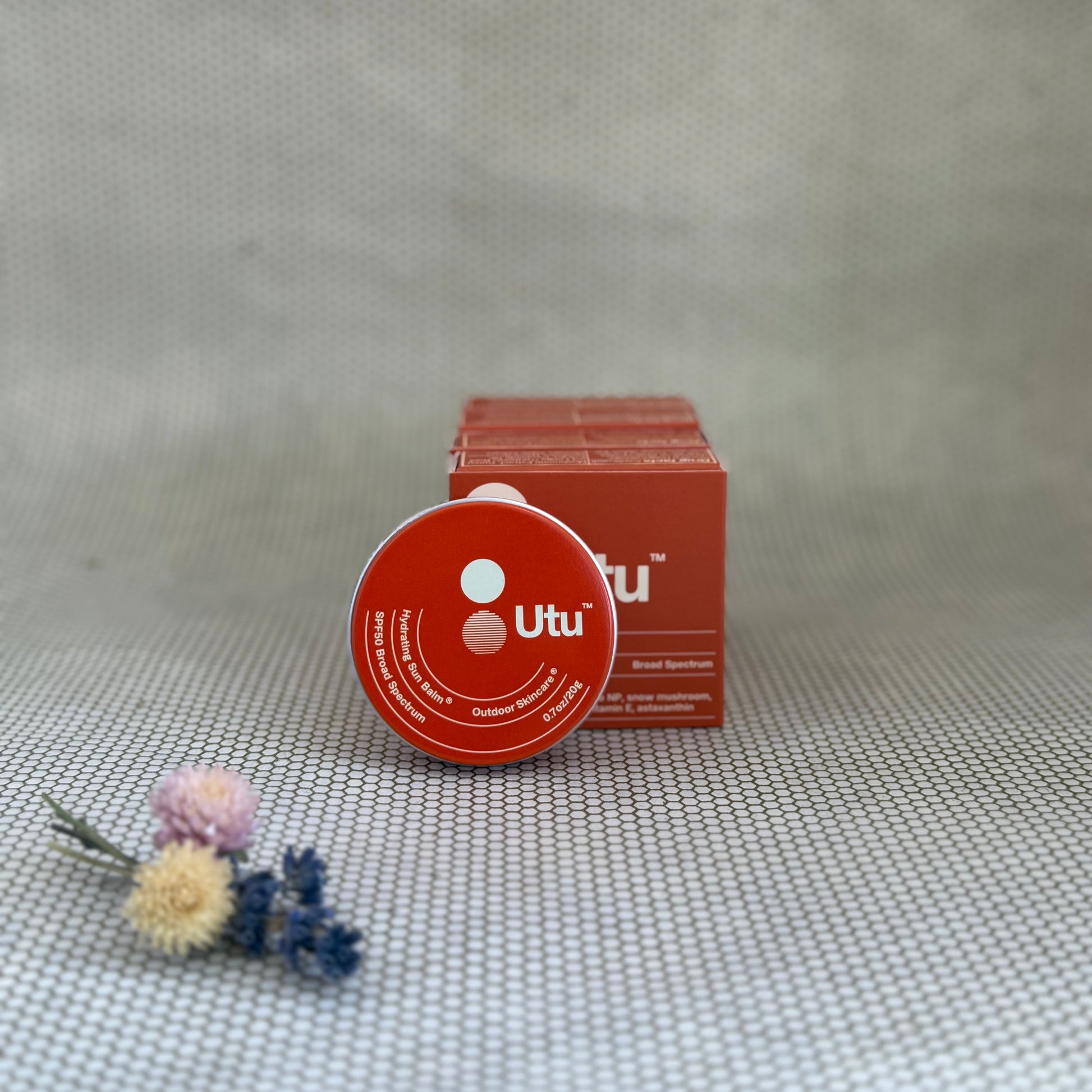 Orange tin of Utu hydrating skin balm and orange packaging on neutral background. 