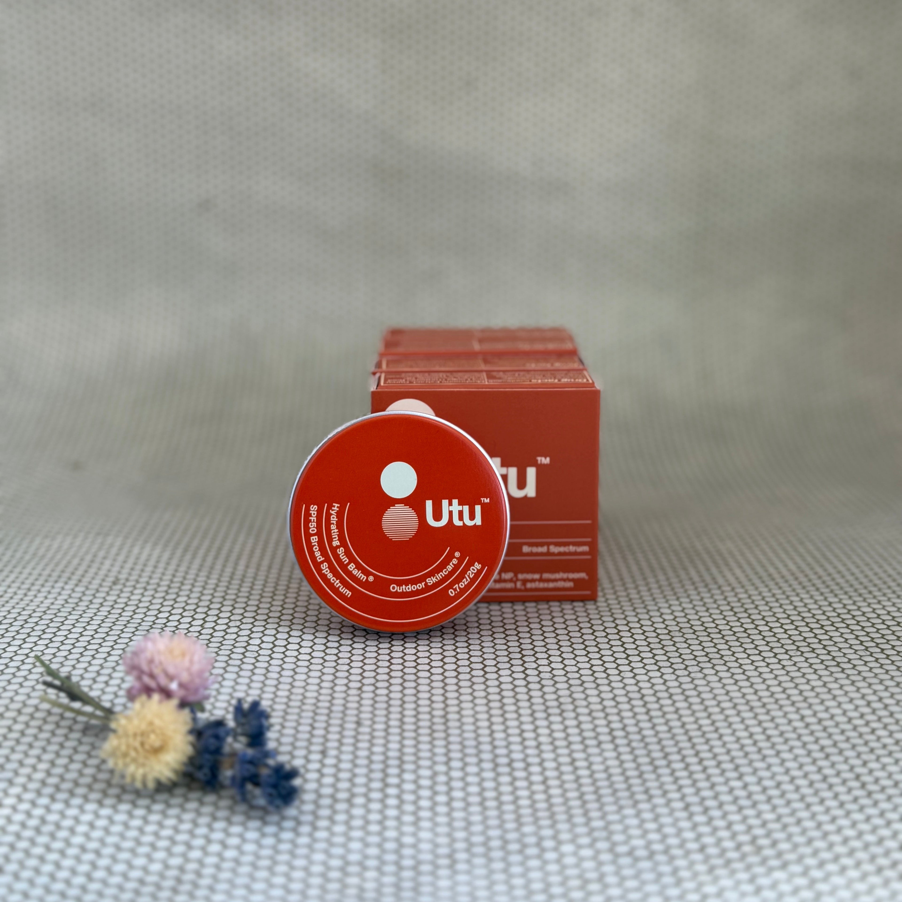 Orange tin of Utu hydrating skin balm and orange packaging on neutral background. 