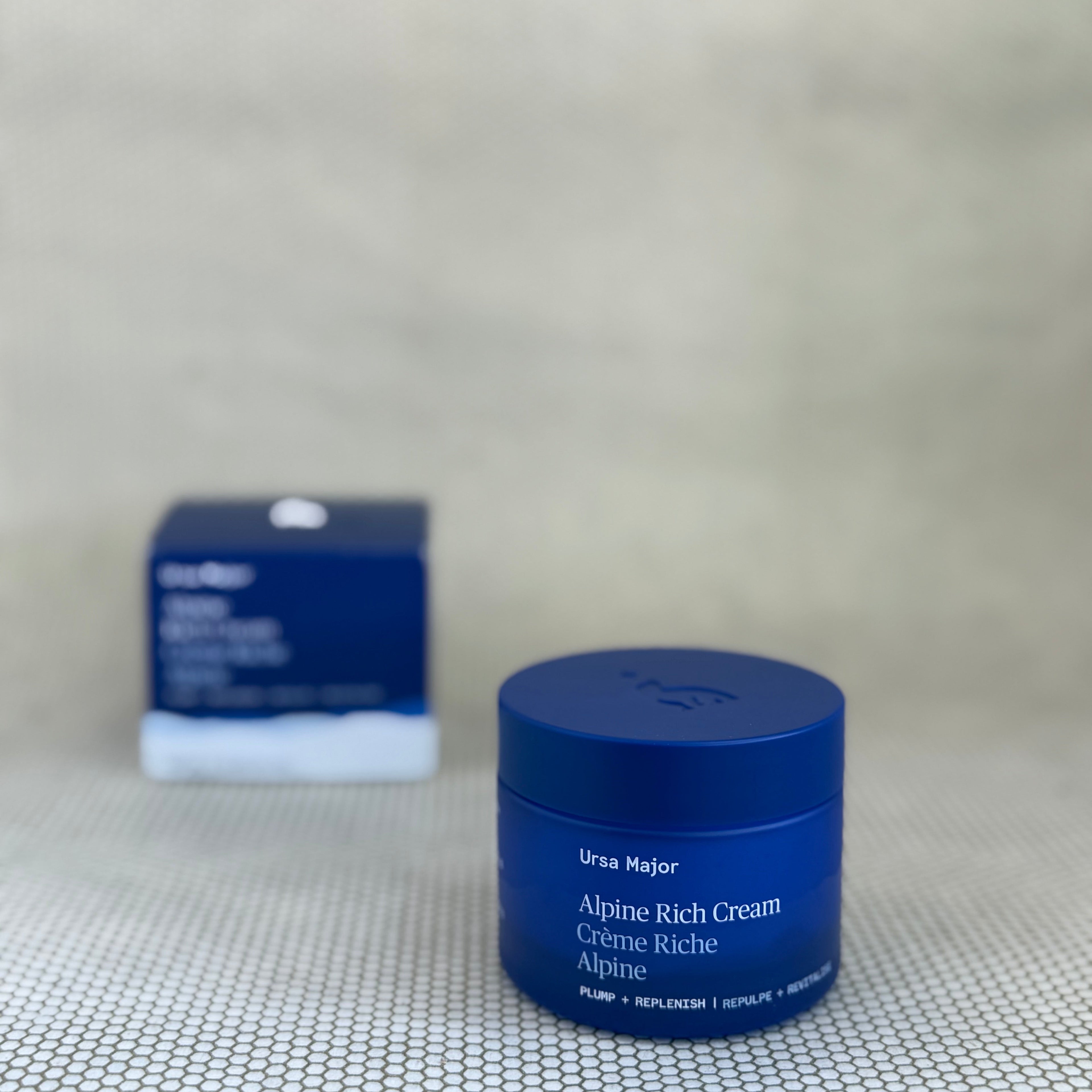 Blue jar of Ursae Major Alpine Rich Cream on a textured surface with a blurred box in the background.