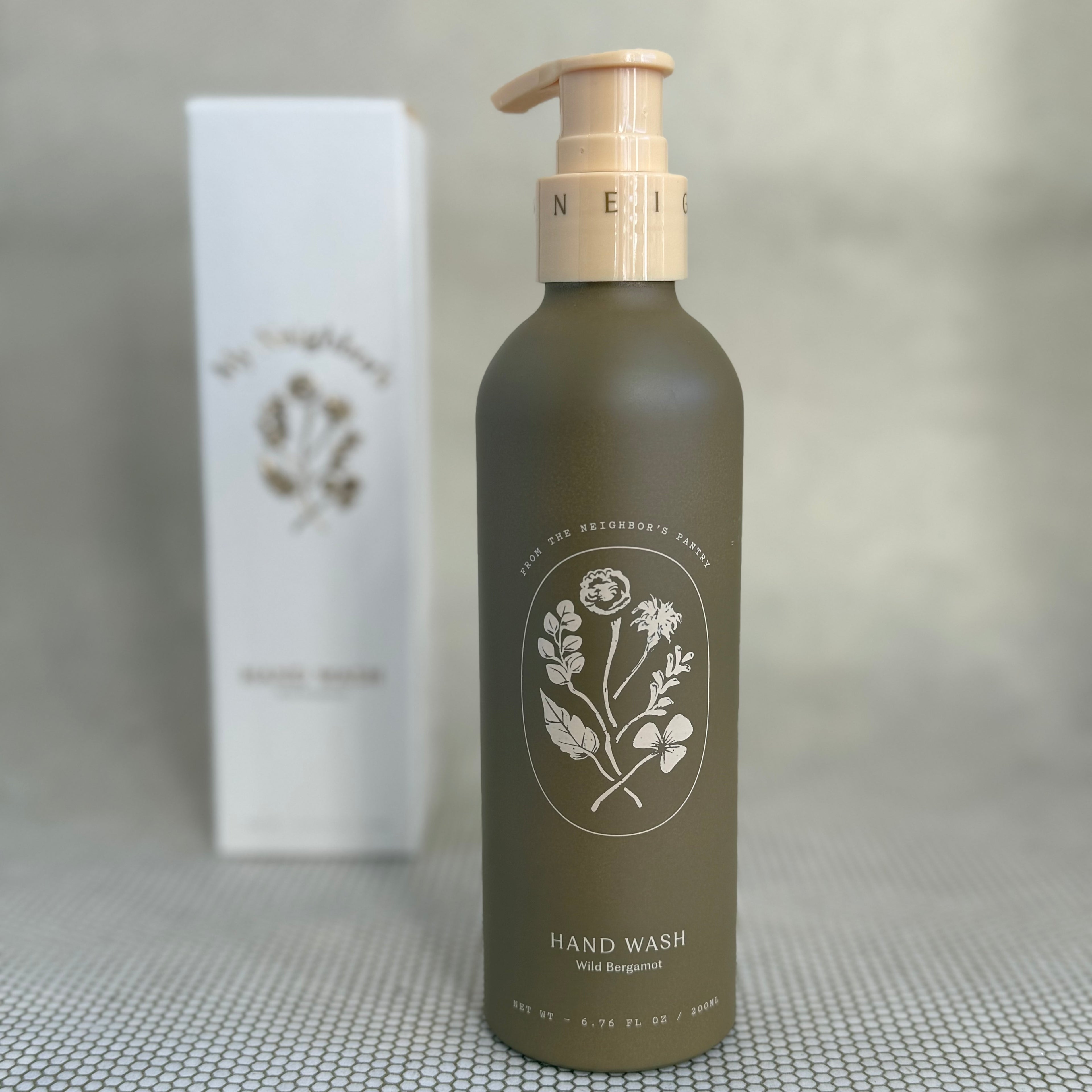 brown pump bottle of My Neighbor's wild bergamot hand wash with floral design and white packaging box in background. 