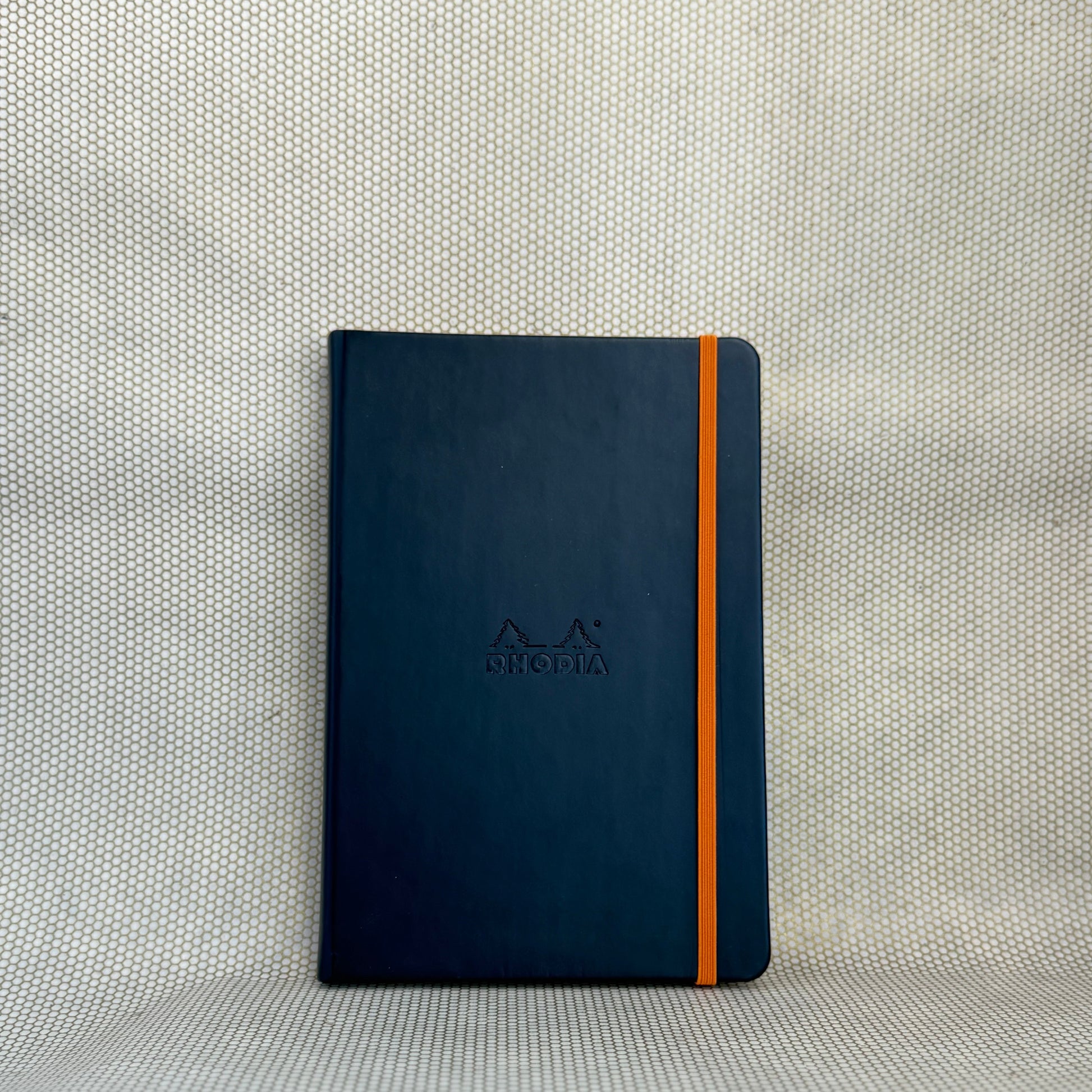 black rhodia notebook A5 with orange elastic band on neutral background. 
