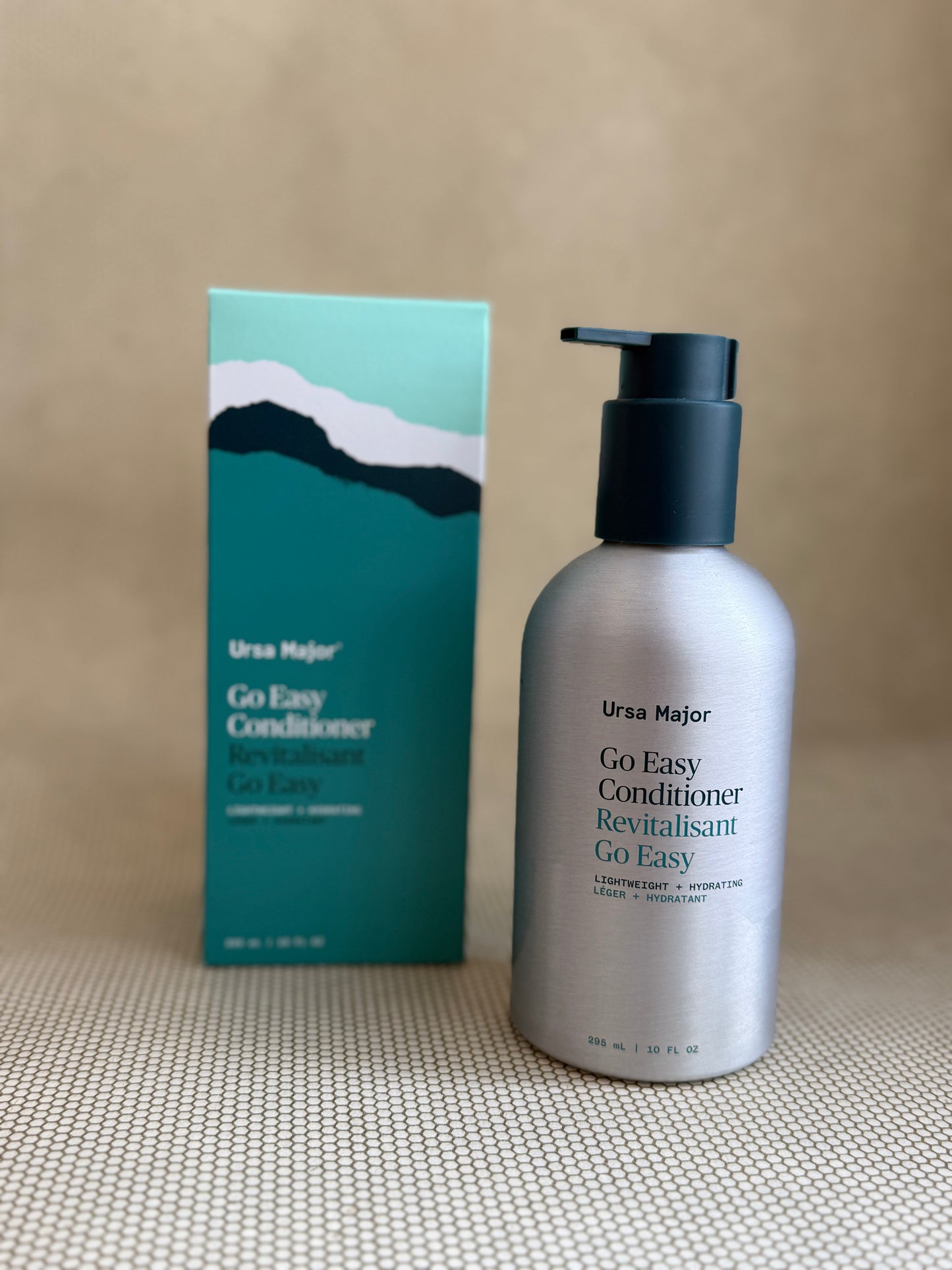 metallic bottle of Ursa Major "go easy" conditioner with pump on neutral background with box.