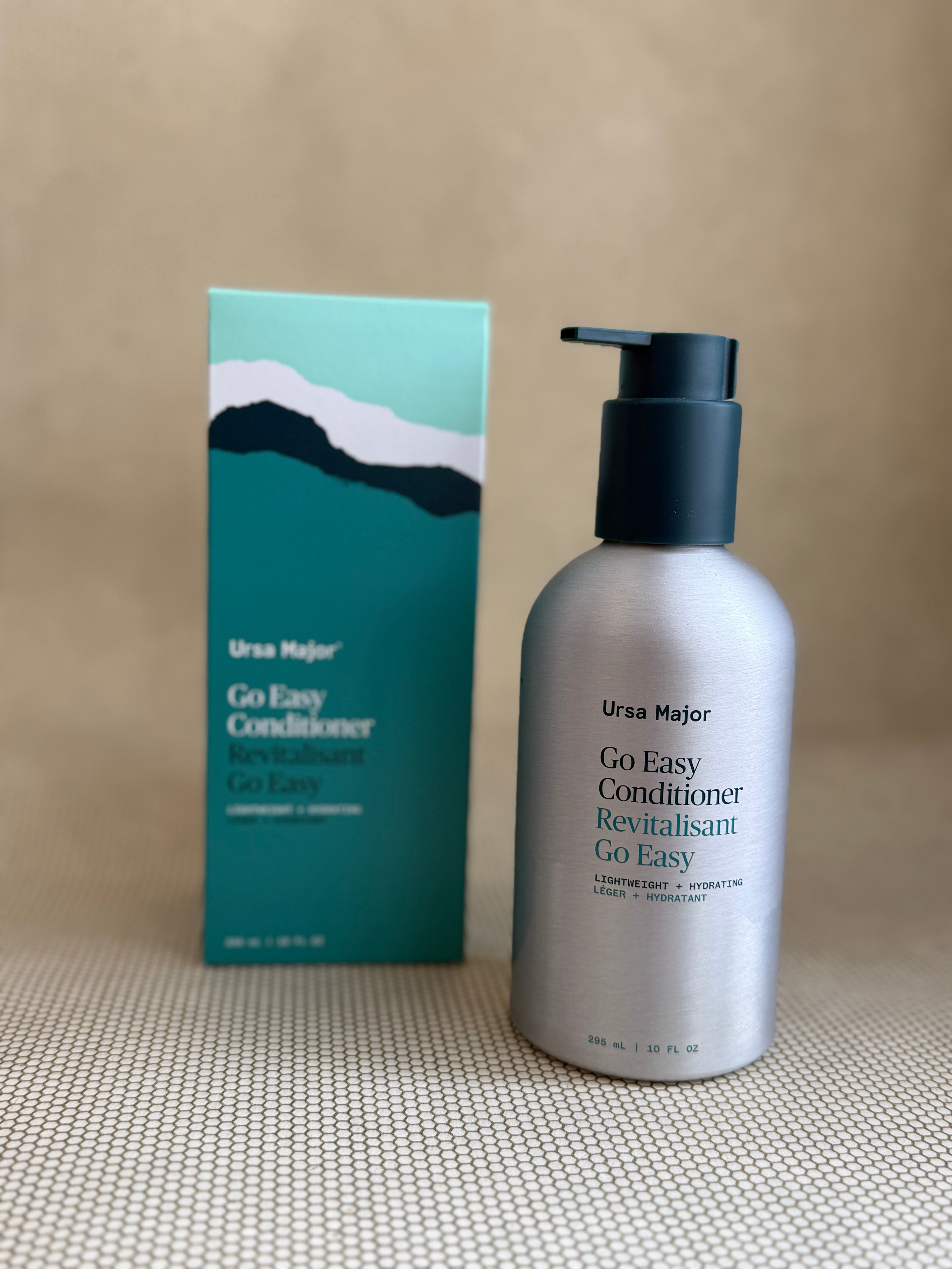 metallic bottle of Ursa Major "go easy" conditioner with pump on neutral background with box.