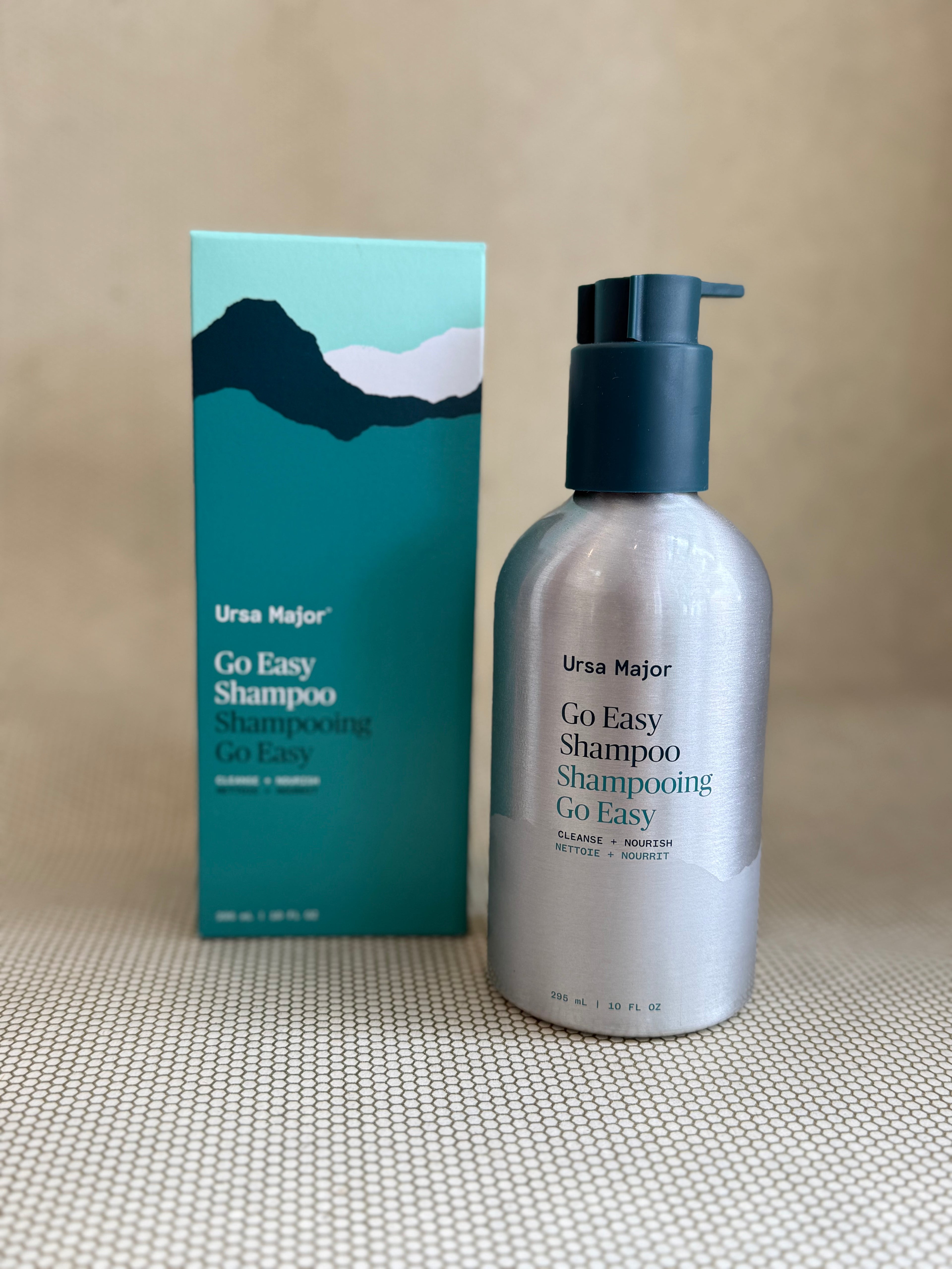 metallic bottle of Ursa Major "go easy" shampoo with pump on neutral background with box. 