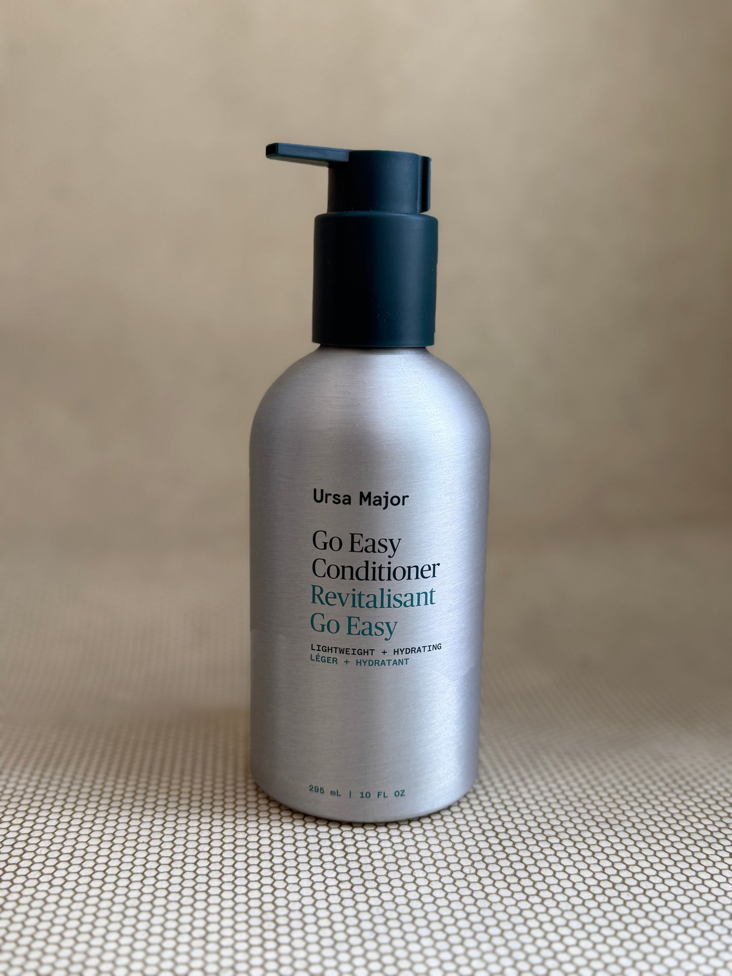metallic bottle of Ursa Major "go easy" conditioner with pump on neutral background.
