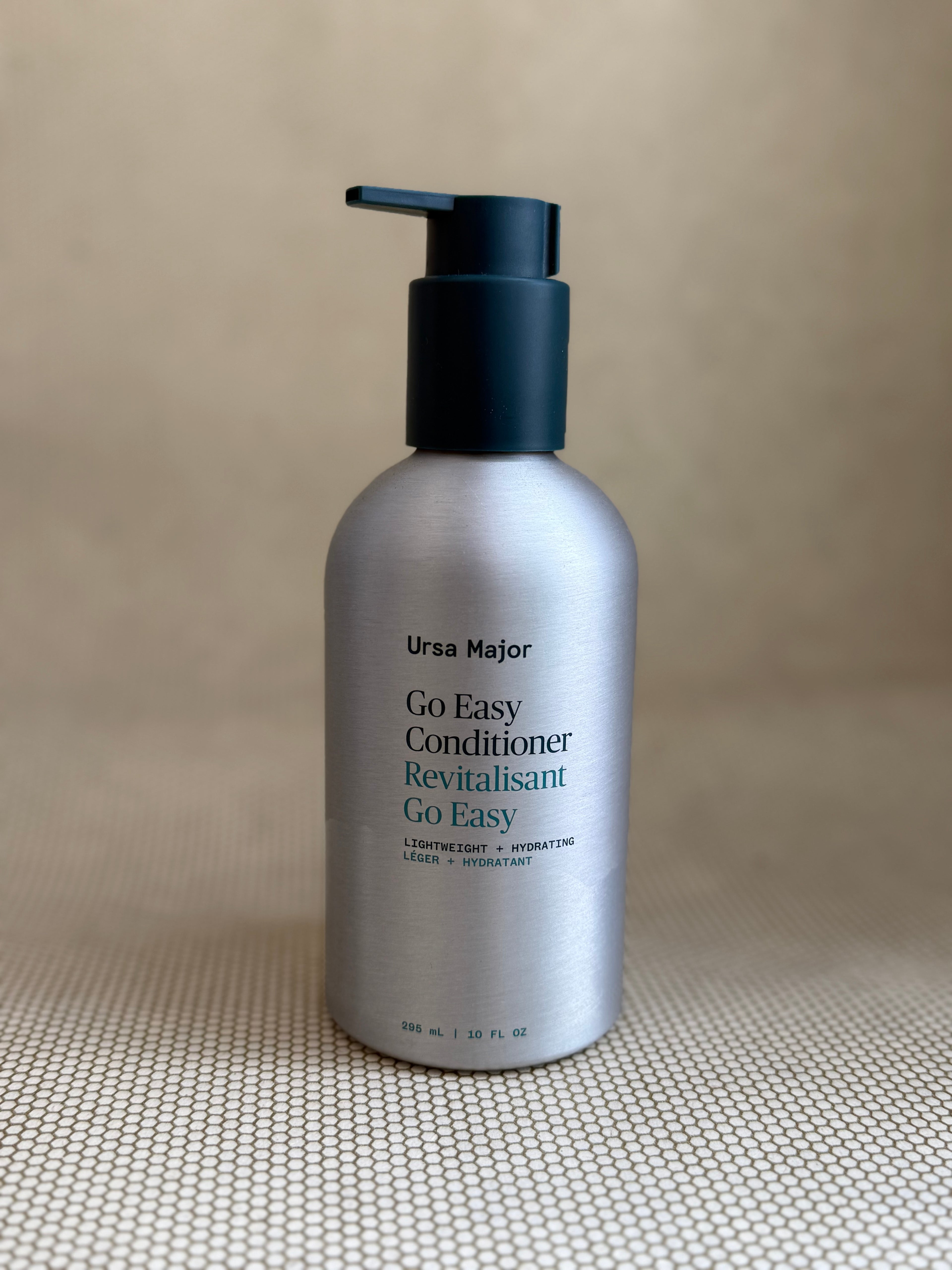 metallic bottle of Ursa Major "go easy" conditioner with pump on neutral background.