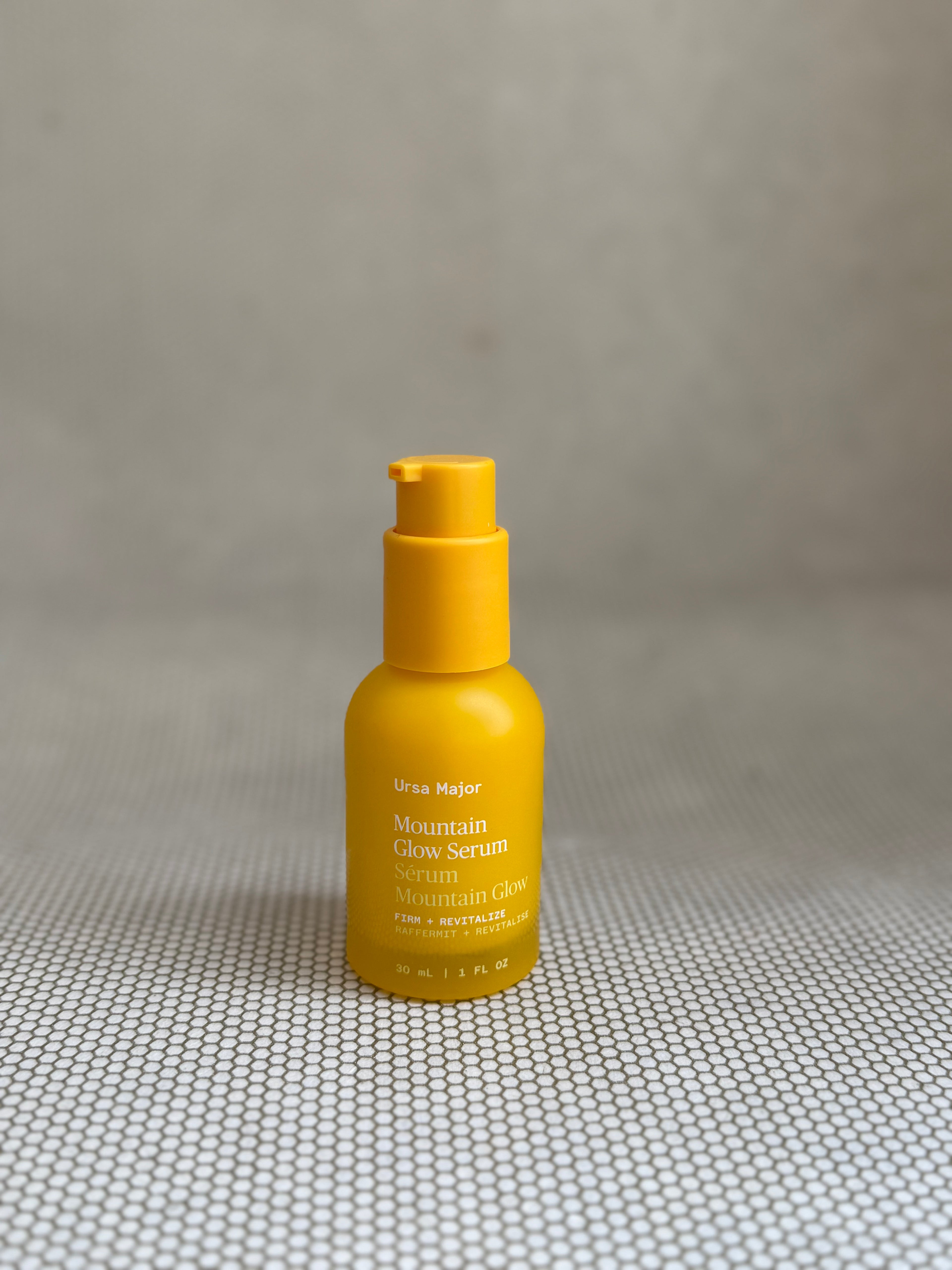 Yellow pump bottle of Ursa Major Mountain Glow Serum on neutral background. 
