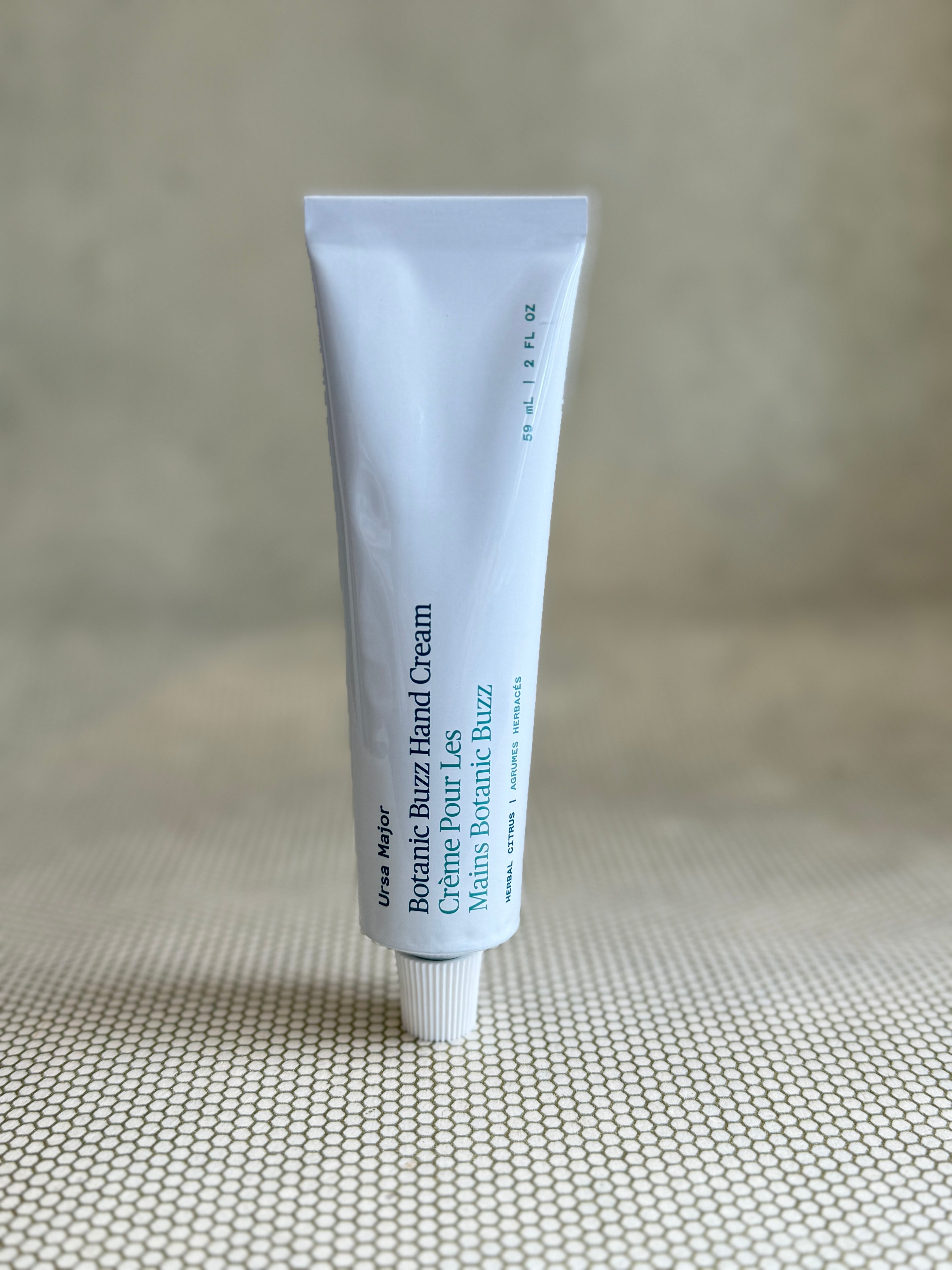 White tube of Ursa Major Botanic Buzz hand cream on neutral background. 