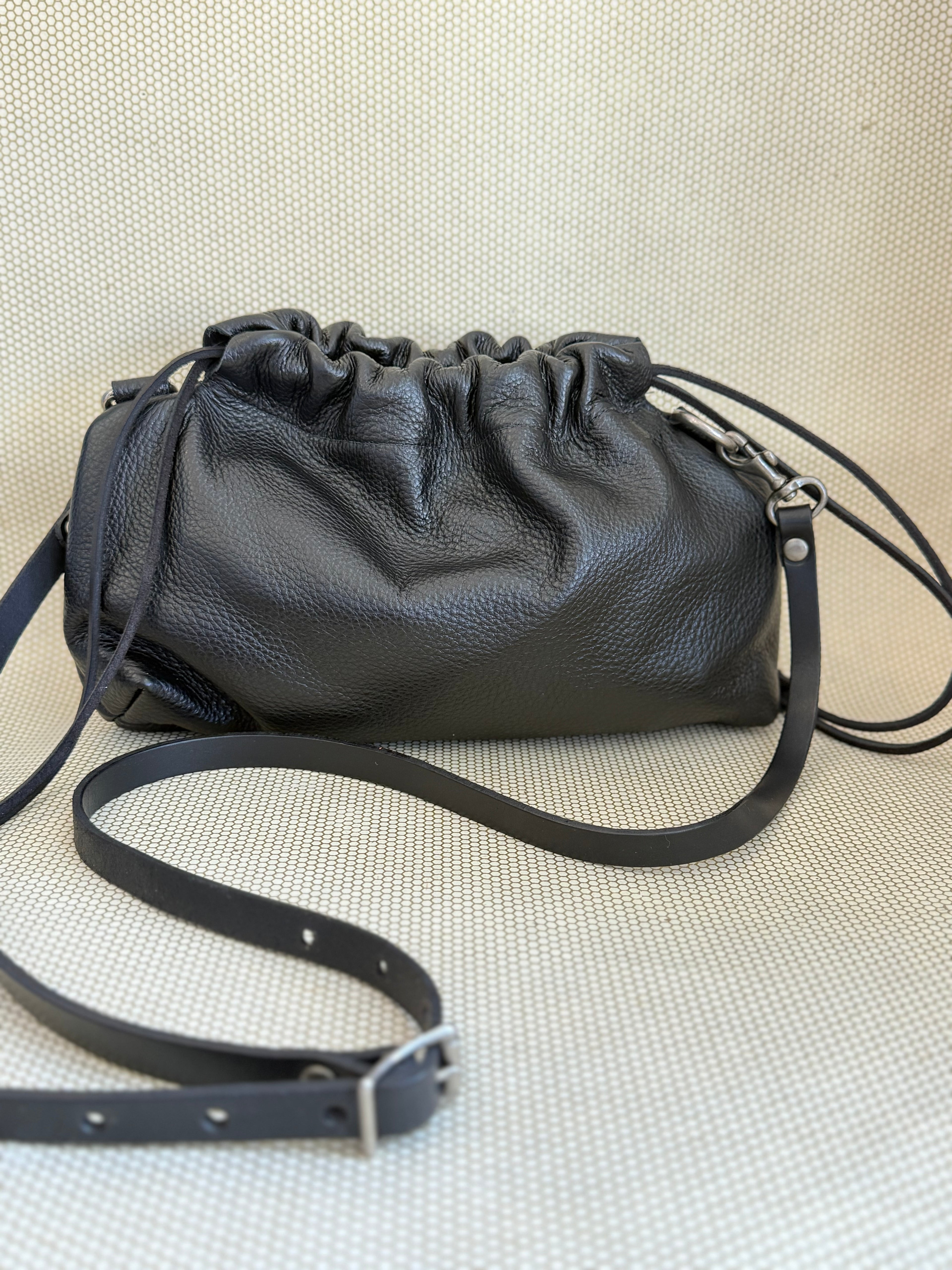 Black leather pouch bag with drawstring and strap on a light gray background.