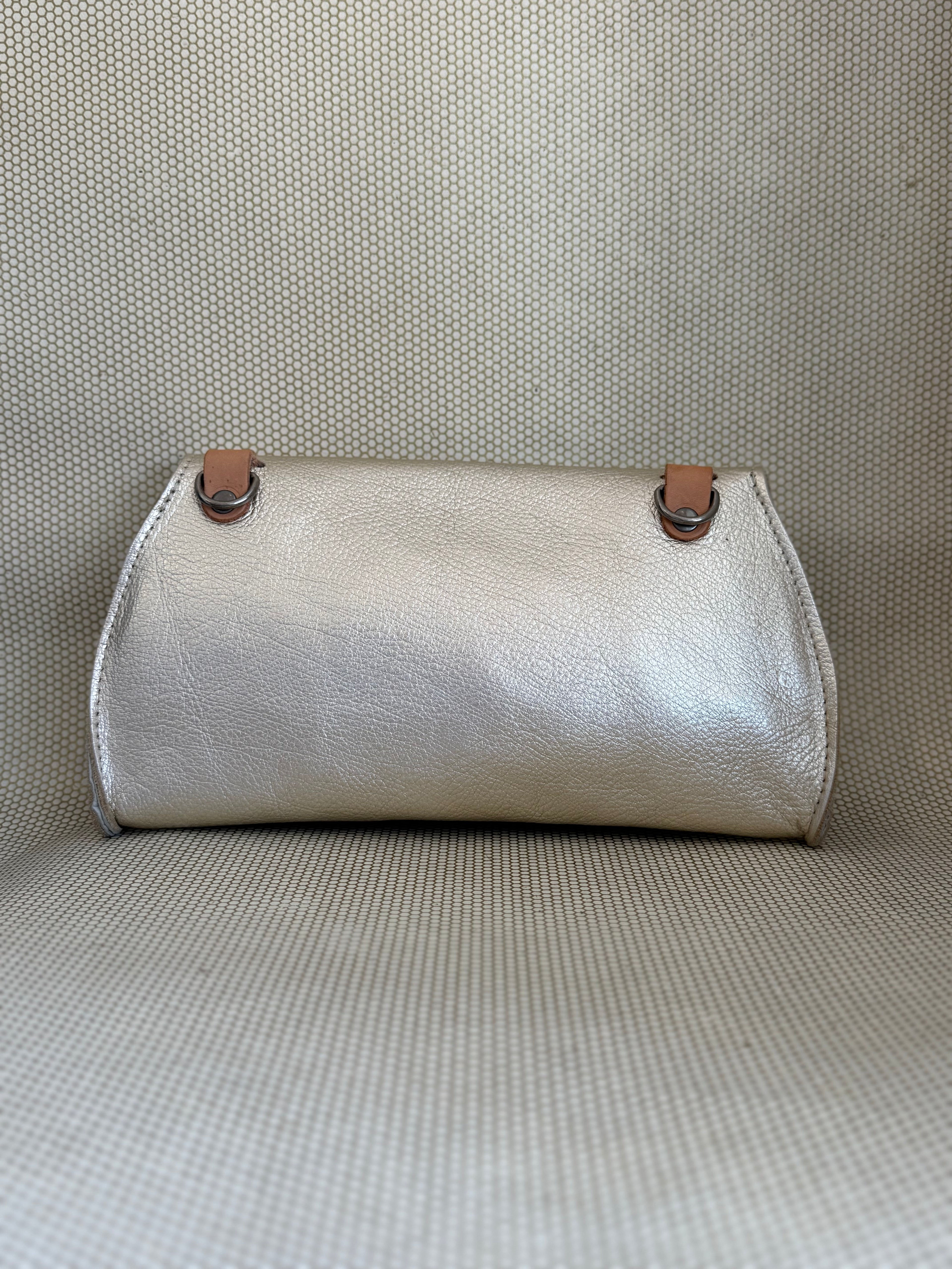 silver Dean leather clutch bag on a textured surface. 