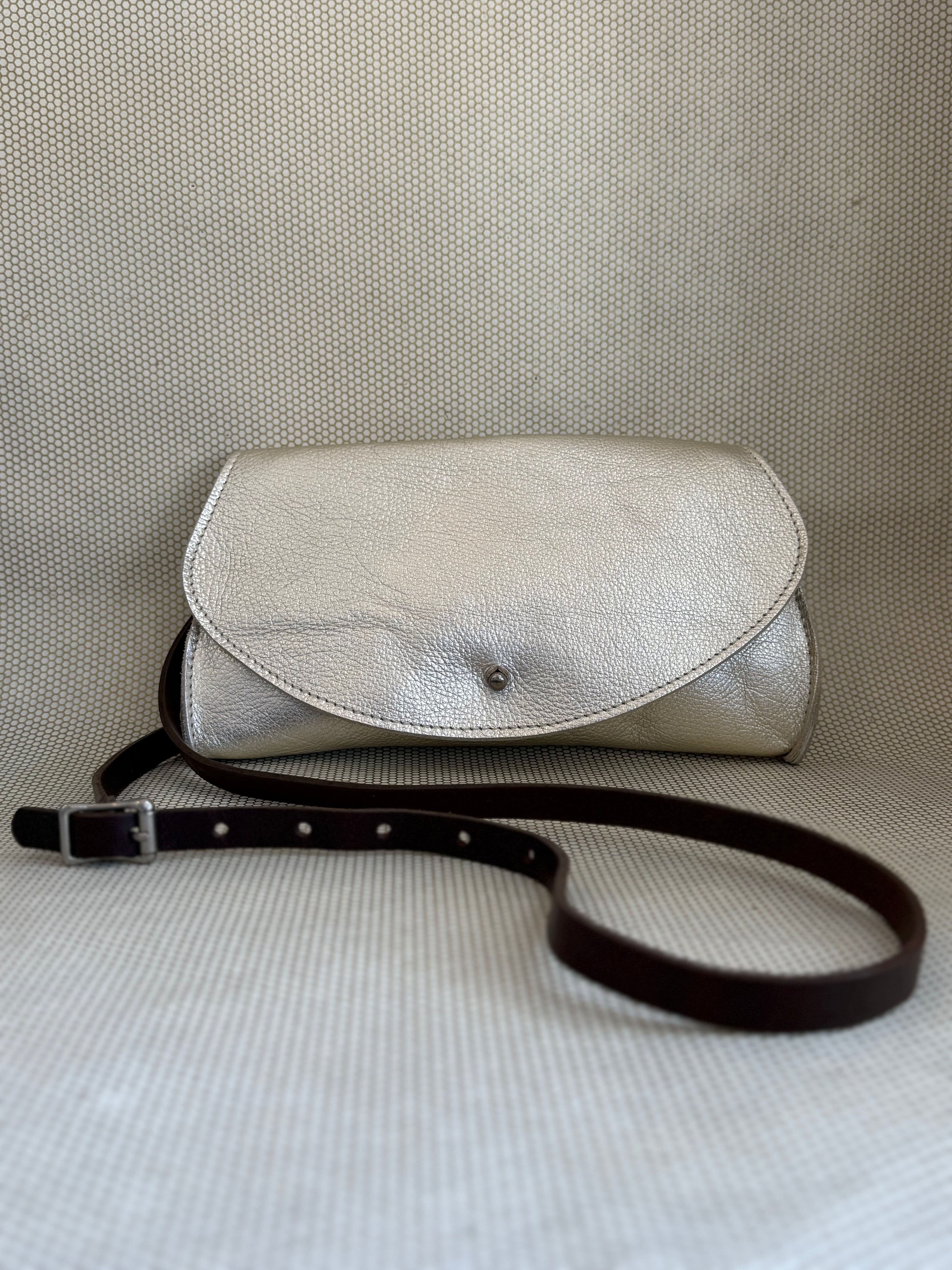 silver Dean leather clutch bag on a textured surface with strap.