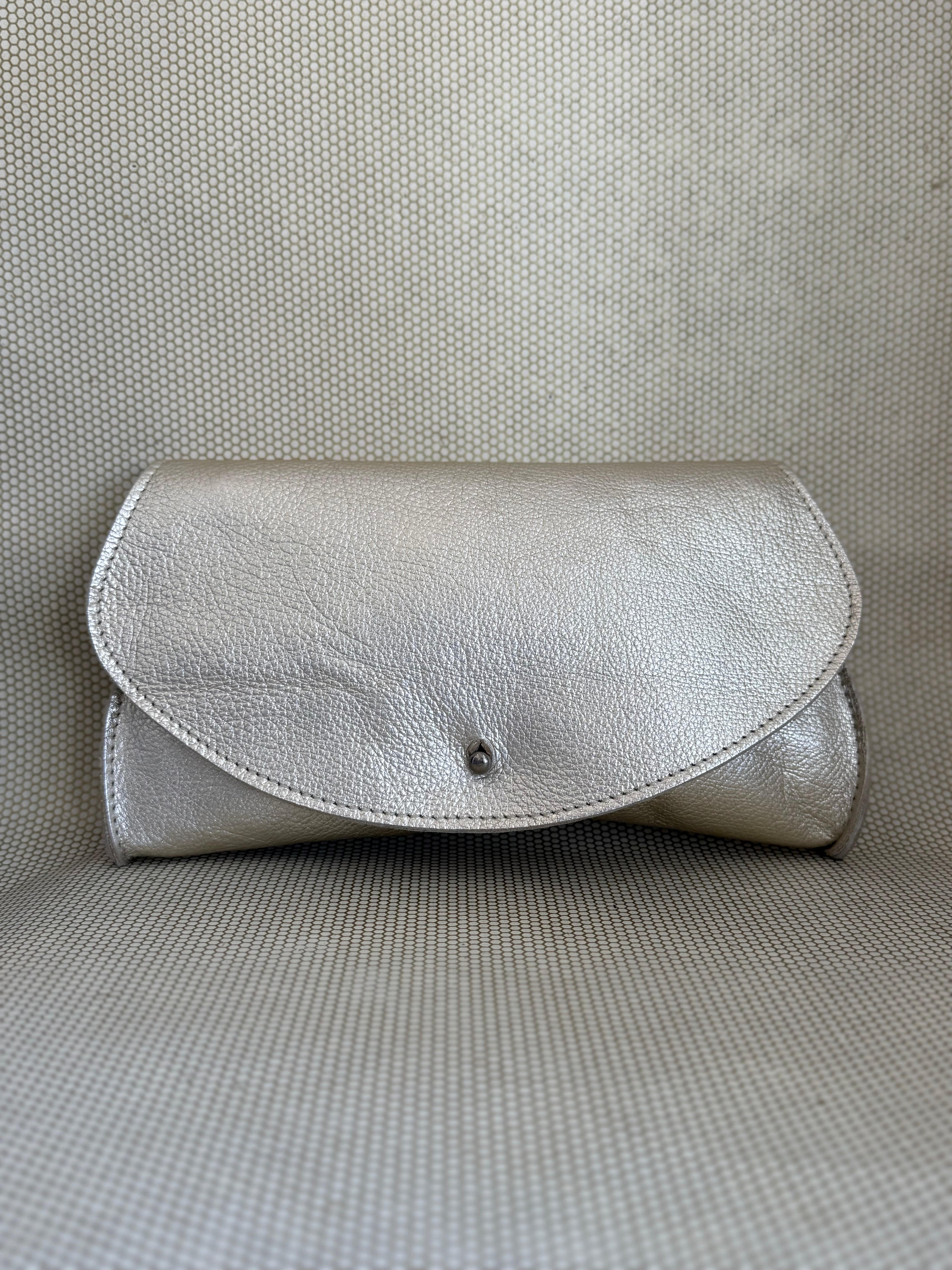 silver Dean leather clutch bag on a textured surface. 