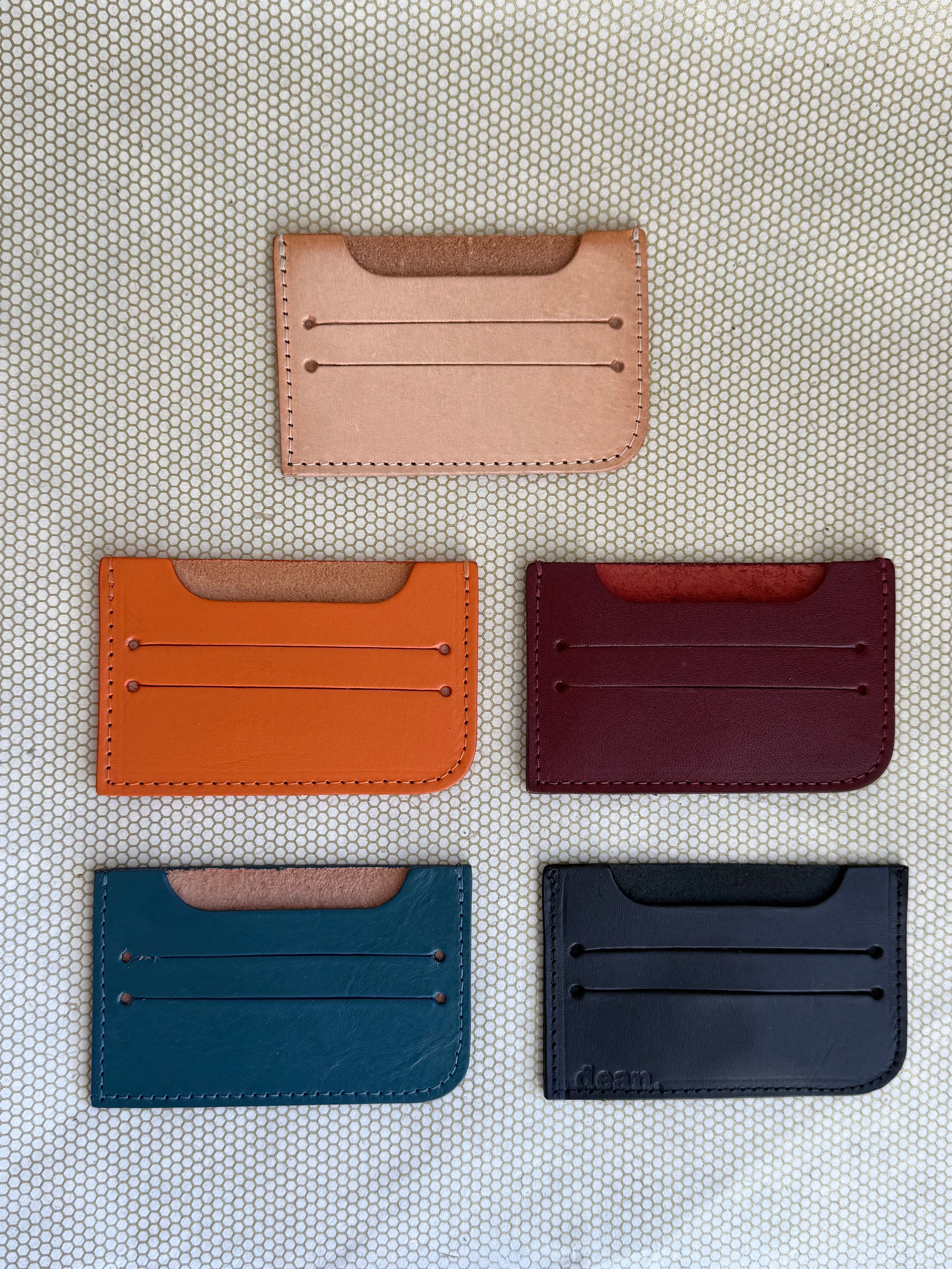 of five leather card holders in different colors on a textured surface