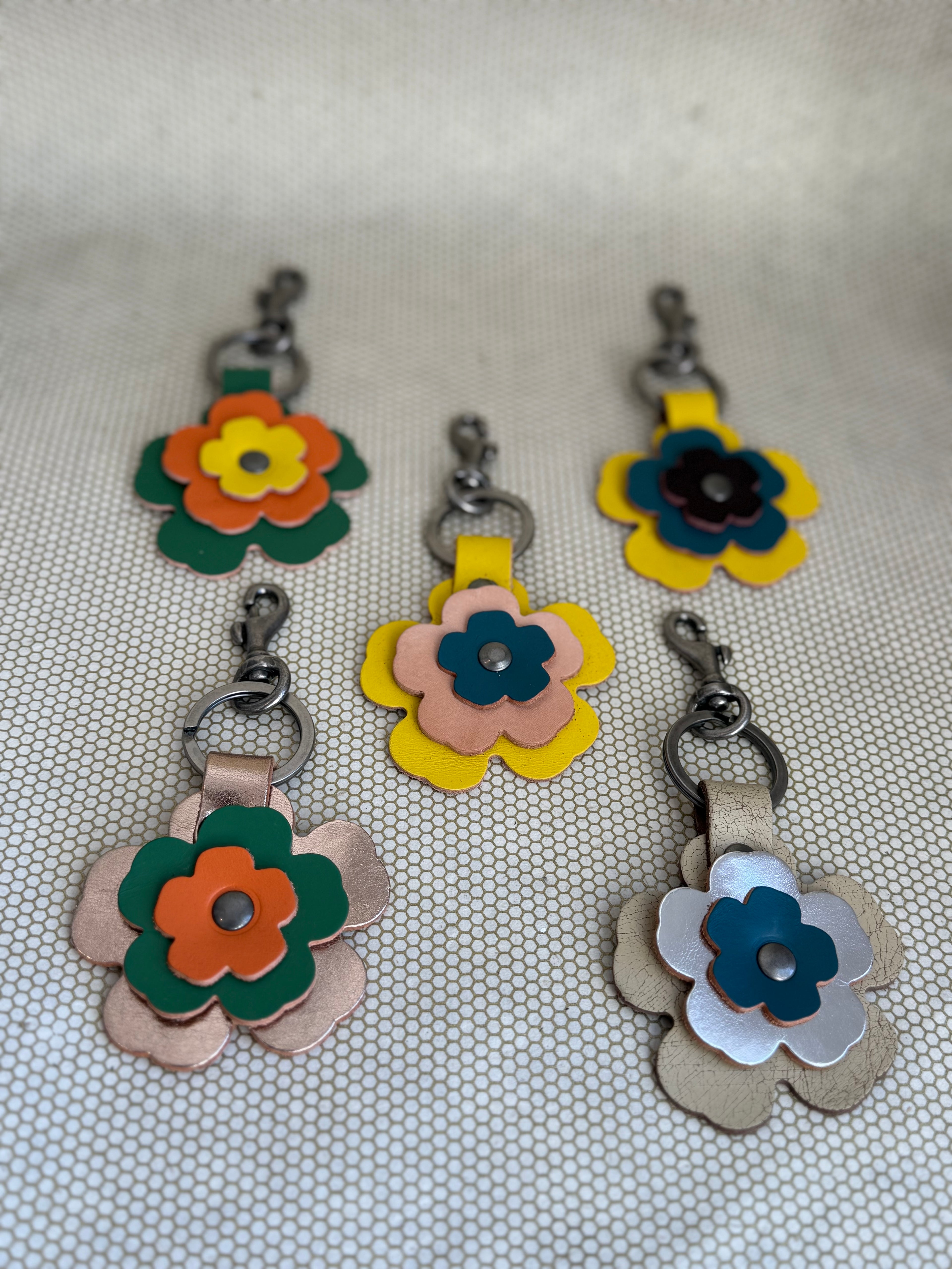 Five colorful flower-shaped leather keychains on a textured surface