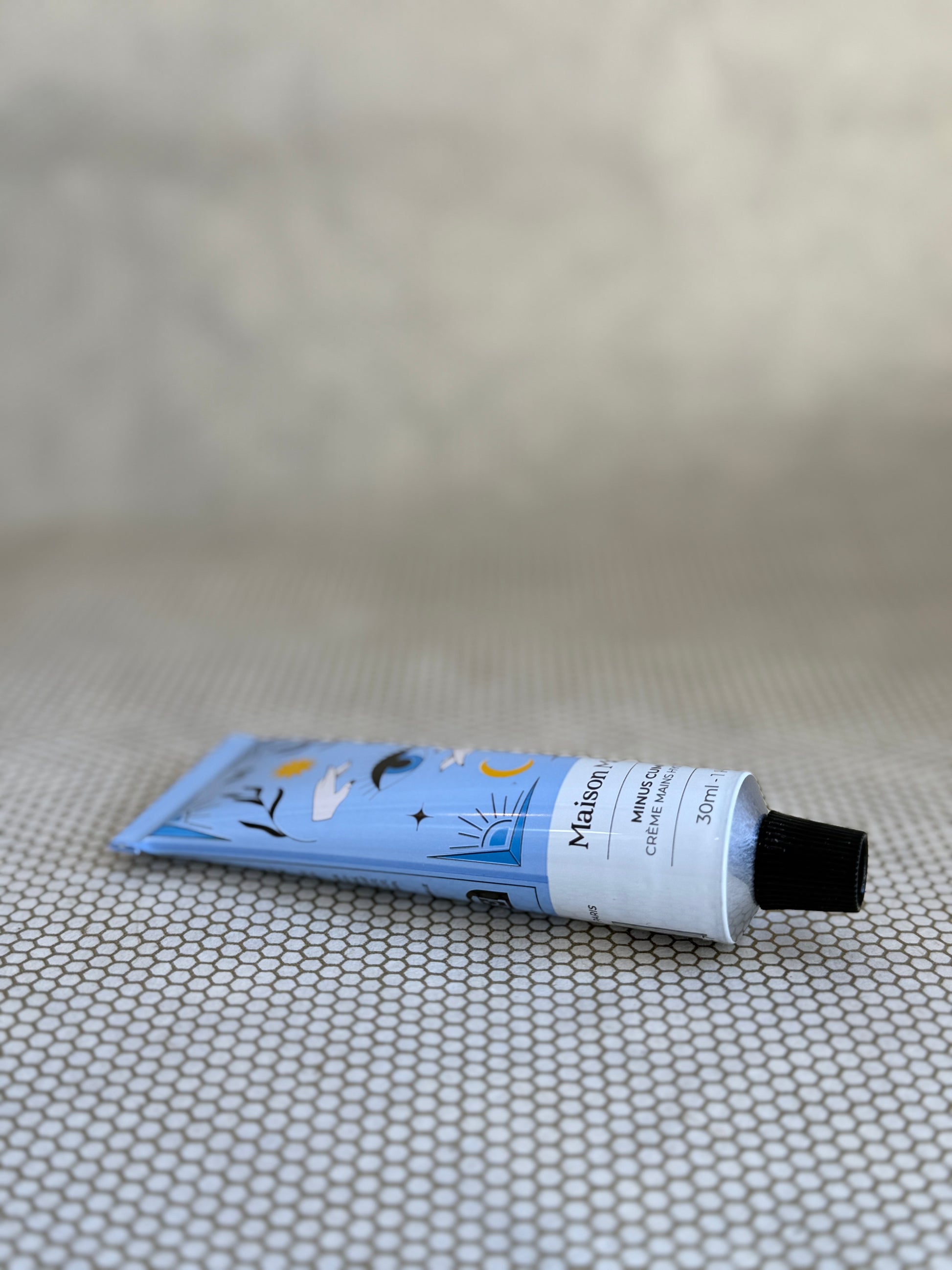 blue tube with artistic design of Maison Matine Minus Cumulus hand cream on neutral background. 
