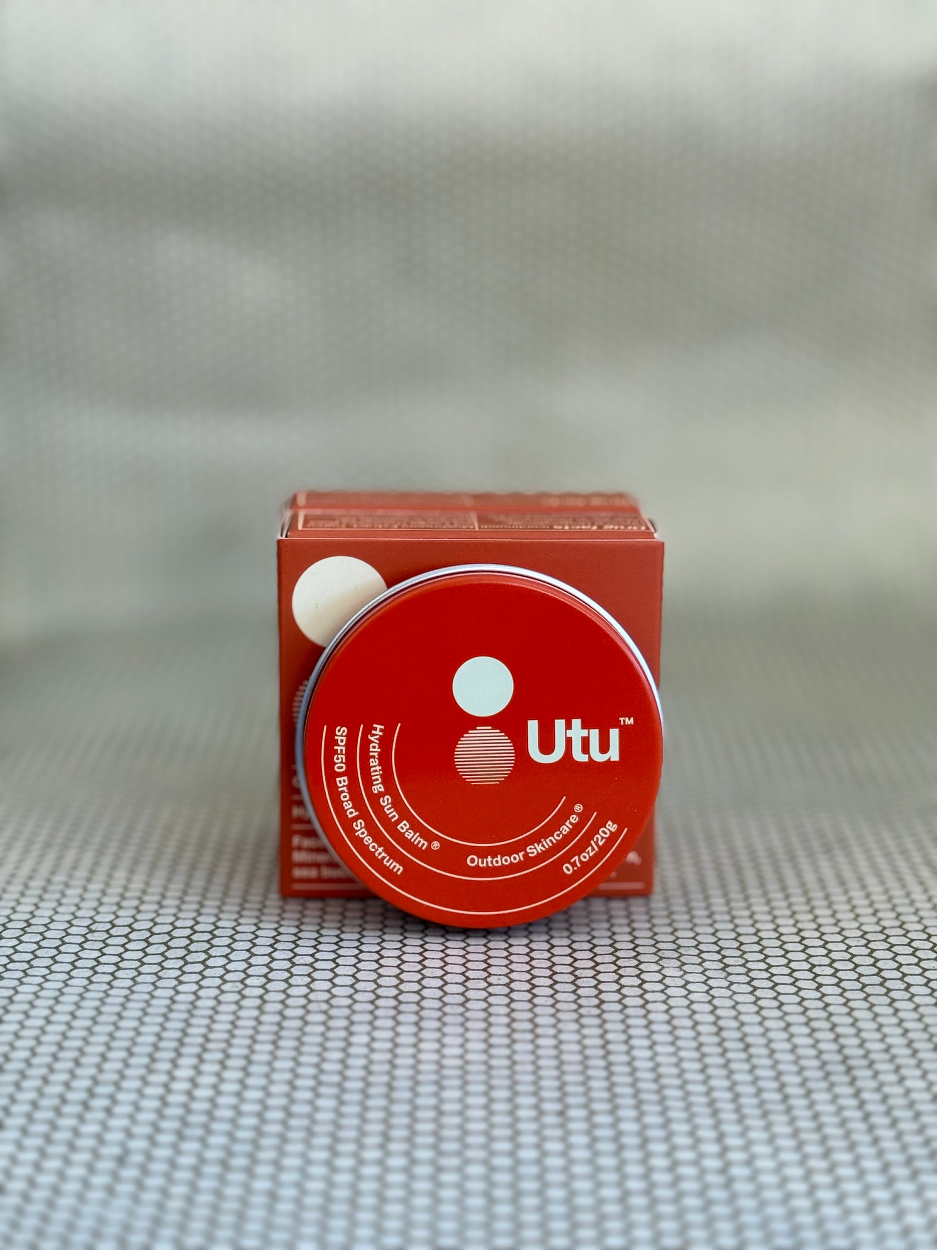 Orange tin of Utu hydrating skin balm and orange packaging on neutral background. 