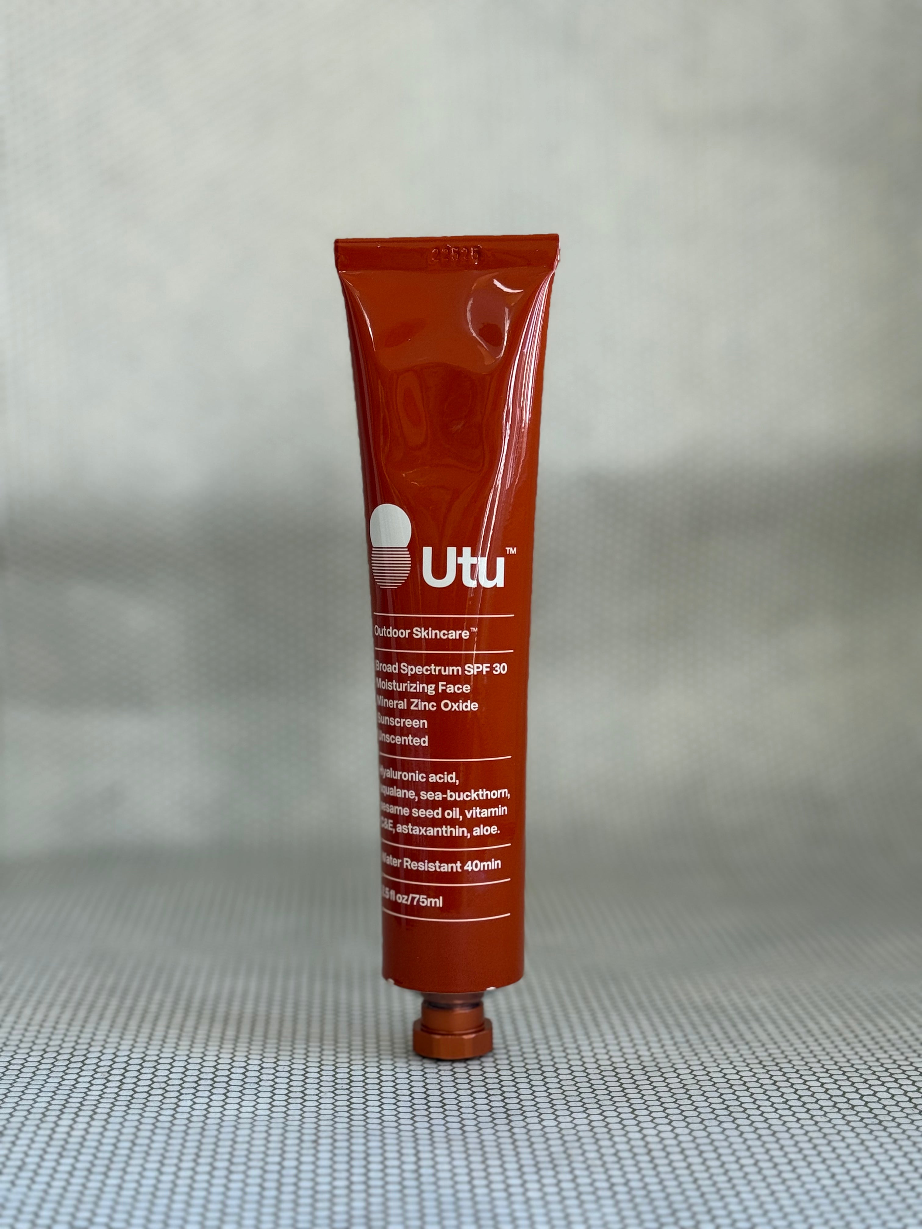 Orange tube of Utu outdoor skincare on a gray background