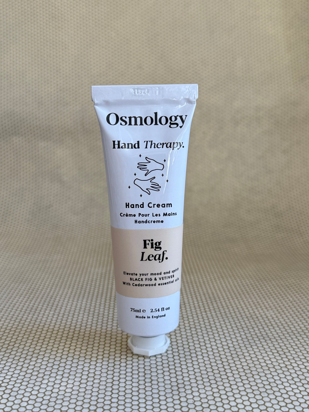 Osmology Fig Leaf hand cream tube on a textured beige surface