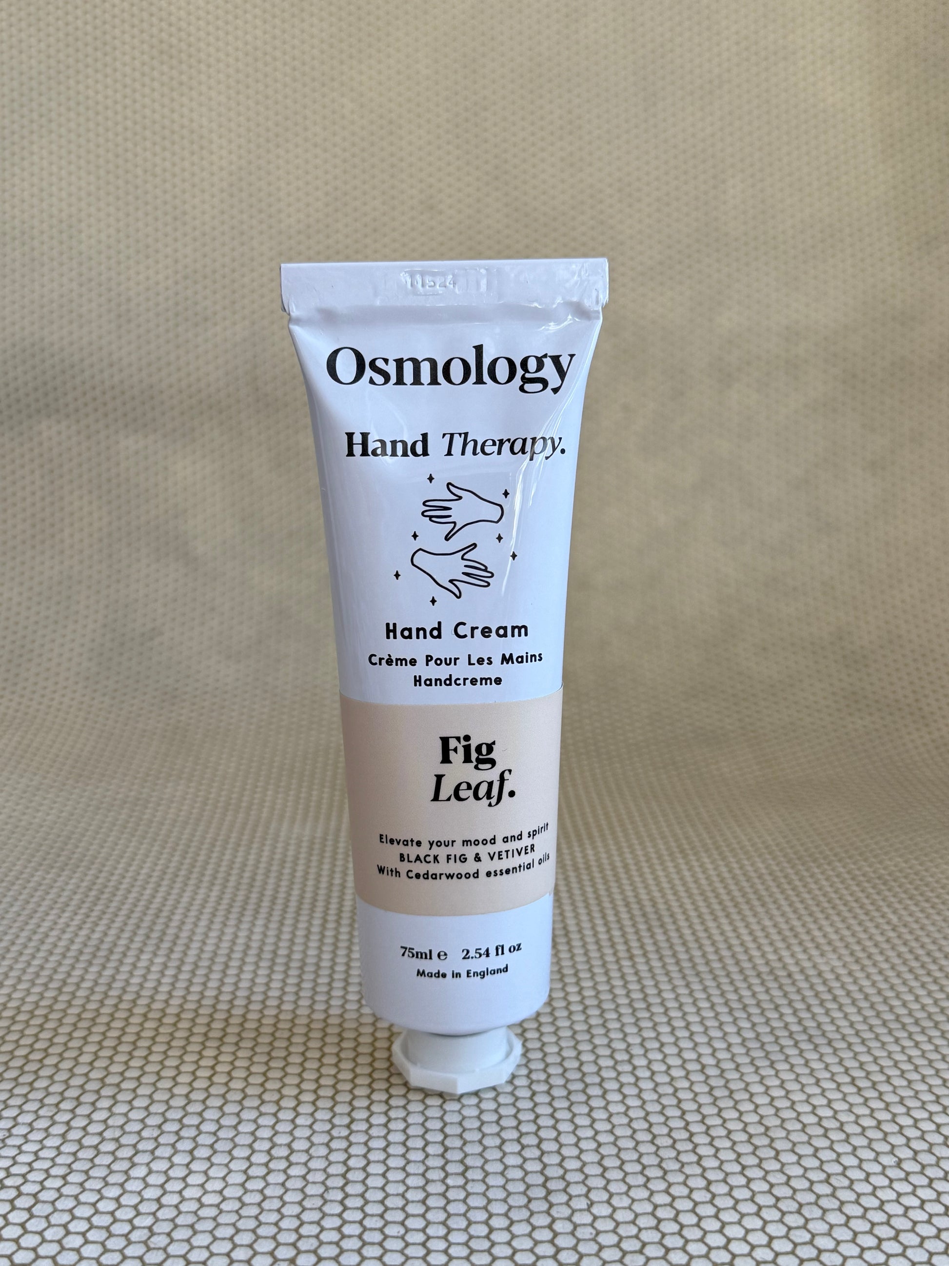 Osmology Fig Leaf hand cream tube on a textured beige surface