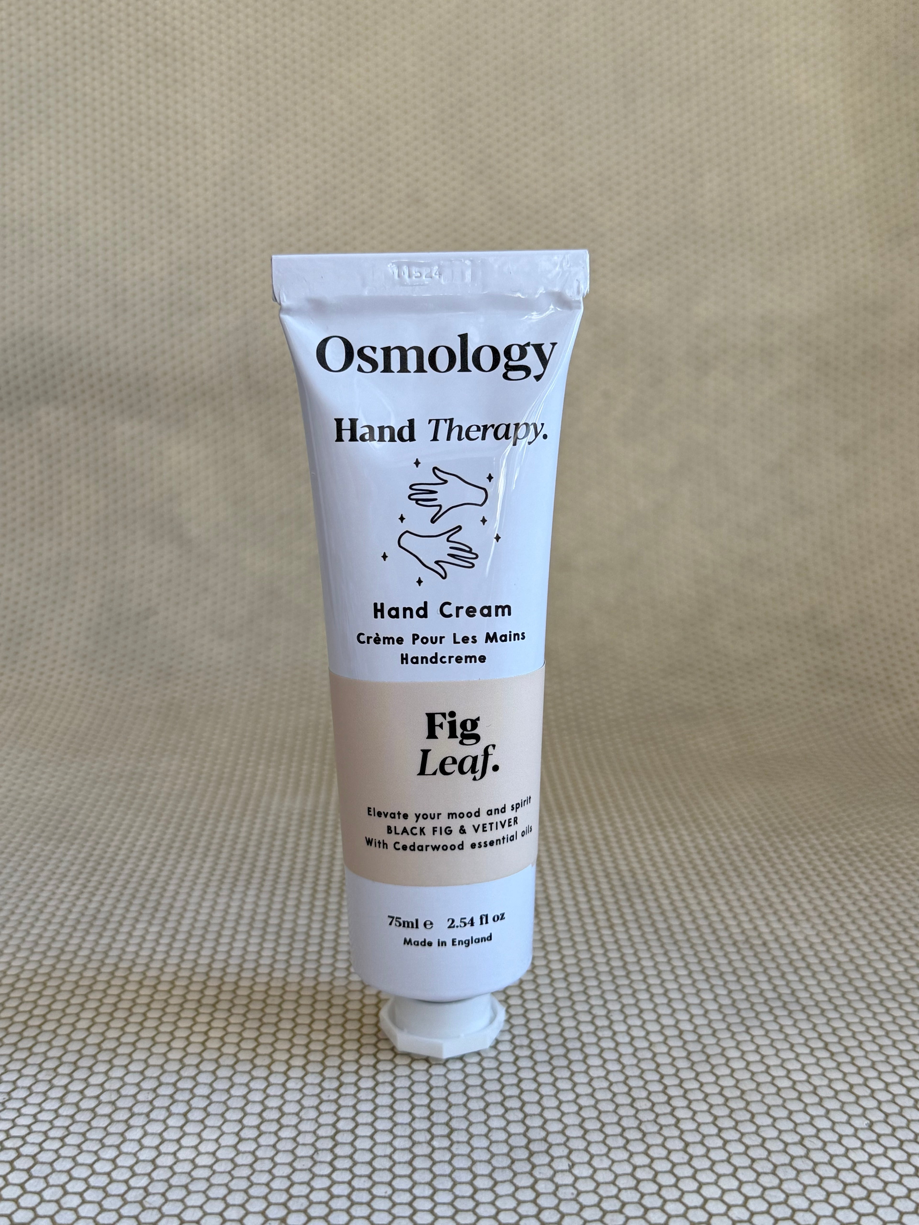 Osmology Fig Leaf hand cream tube on a textured beige surface
