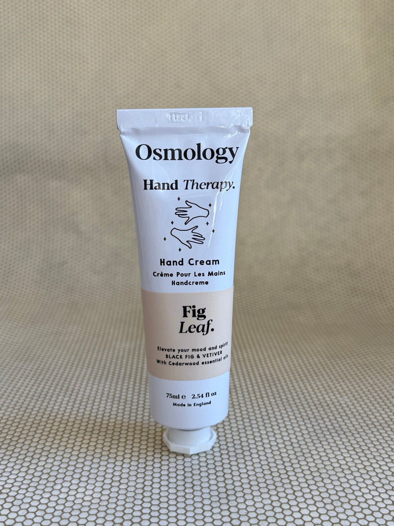 Osmology Fig Leaf hand cream tube on a textured beige surface