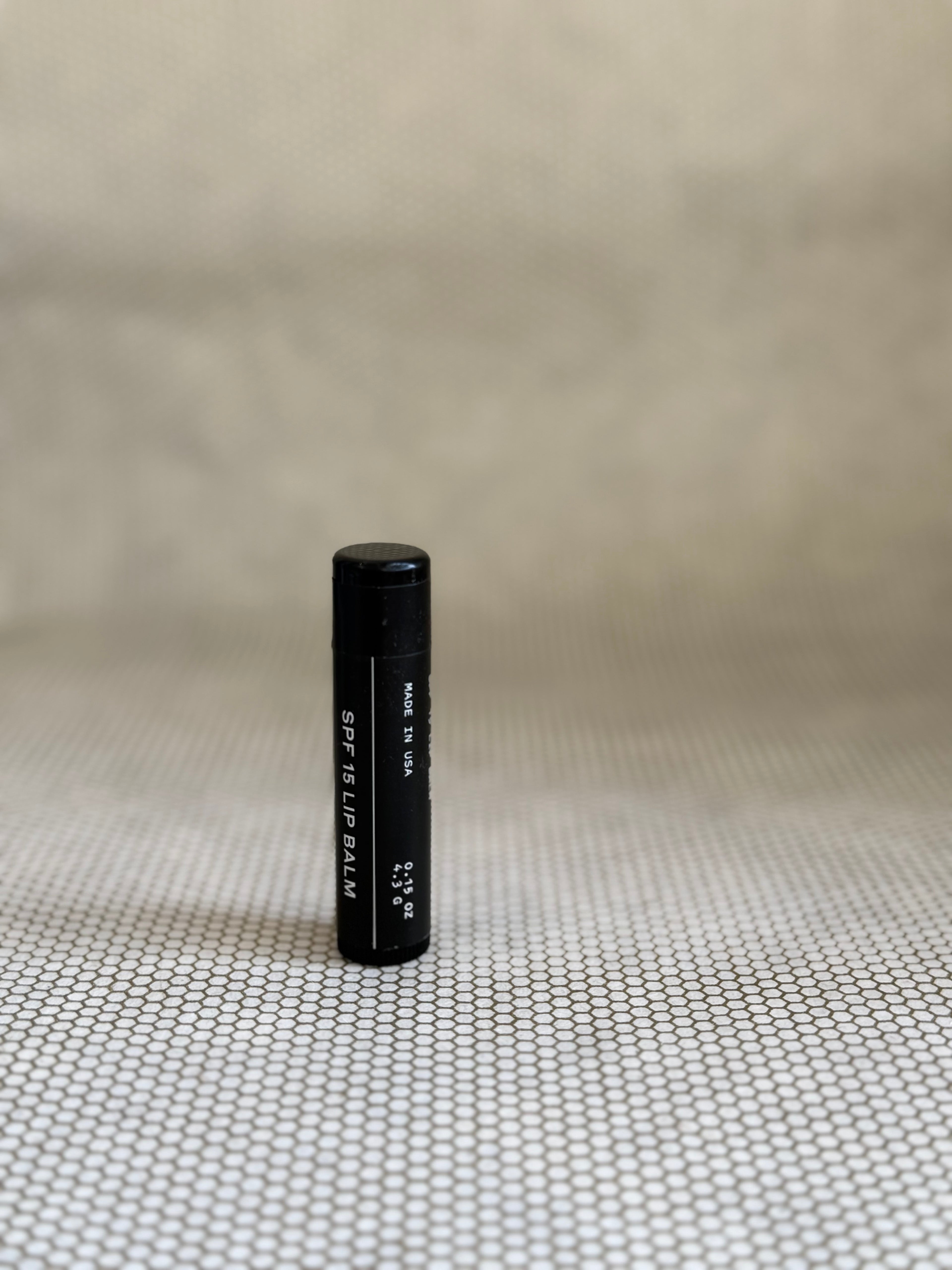 Black cylindrical Preston SPF Lip Balm on a textured beige surface