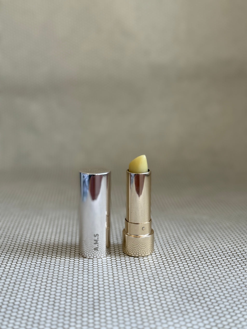 Activist manuka lip balm in silver and gold colored lipstick applicator on neutral background. 