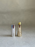 Activist manuka lip balm in silver and gold colored lipstick applicator on neutral background. 
