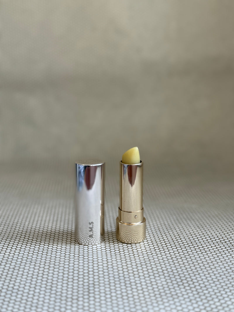 Activist manuka lip balm in silver and gold colored lipstick applicator on neutral background. 