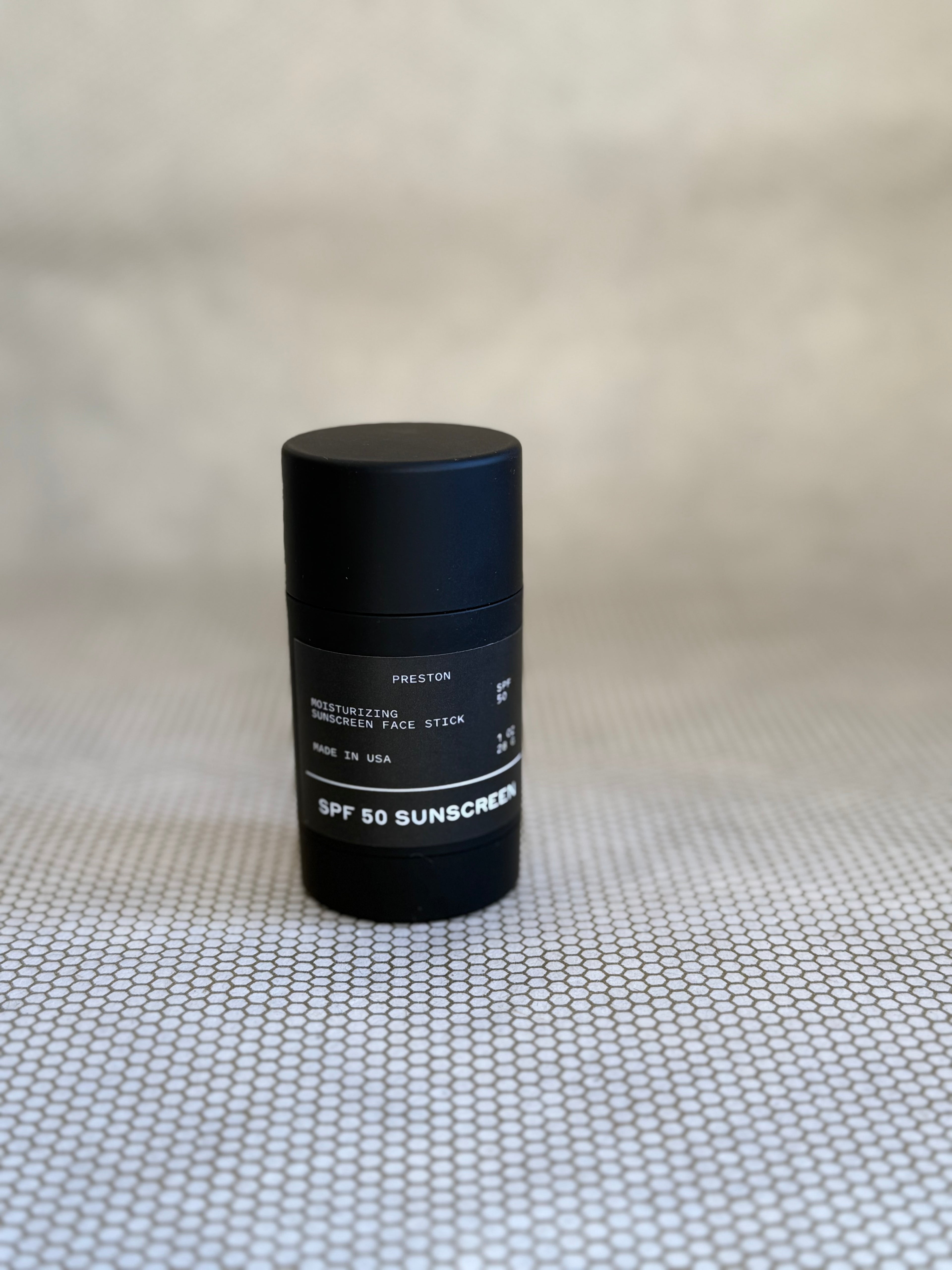 Black Preston SPF 50 sunscreen stick on a textured beige surface