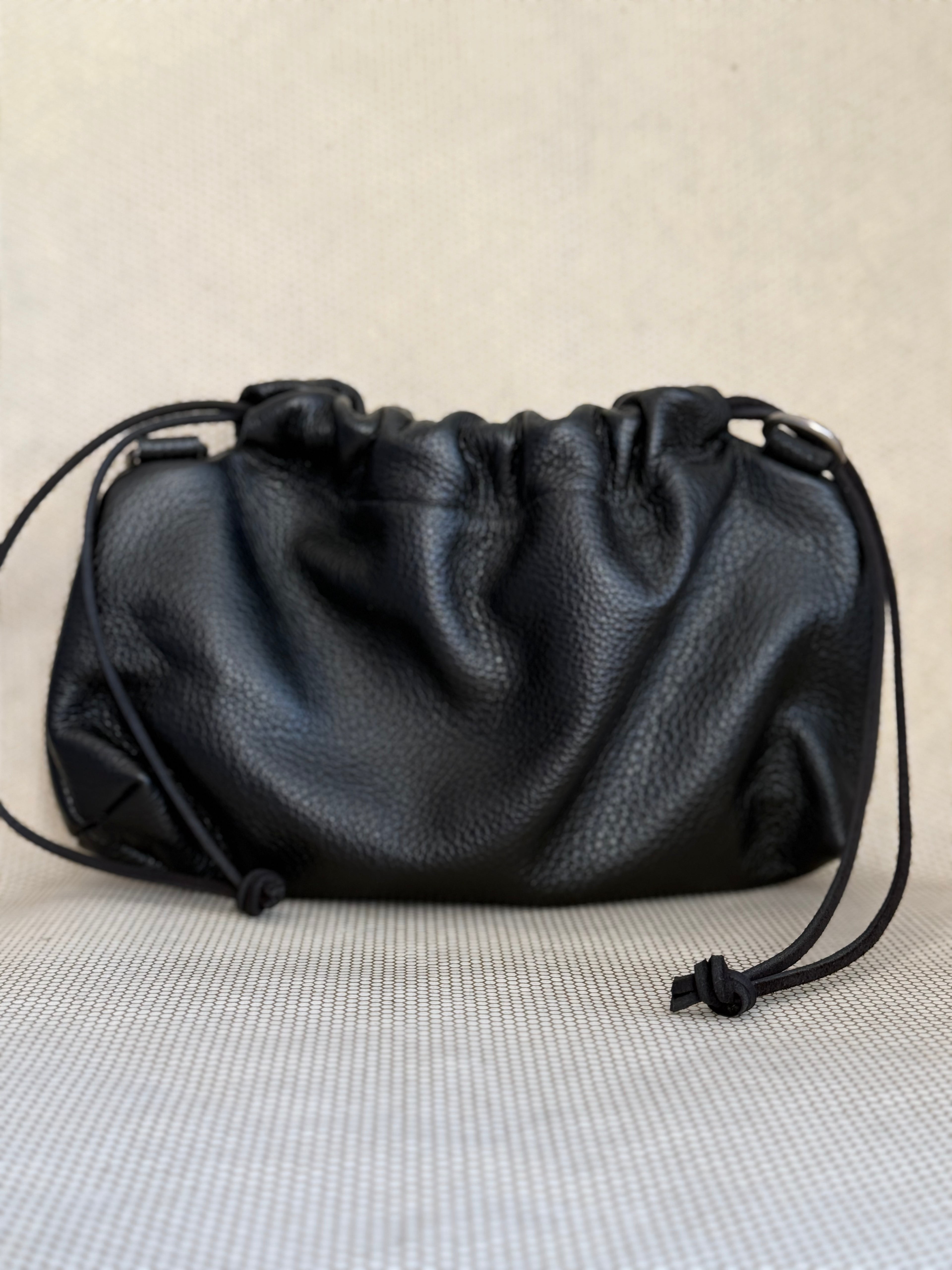 Black leather pouch bag with drawstring and strap on a light gray background.