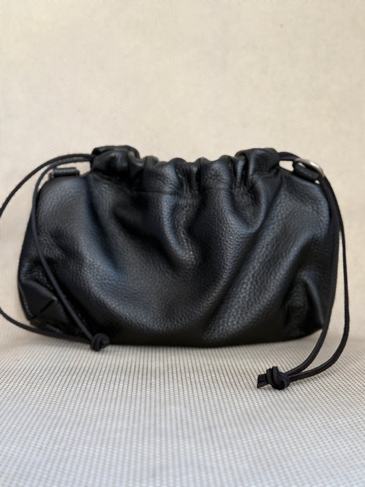 Black leather pouch bag with drawstring and strap on a light gray background.