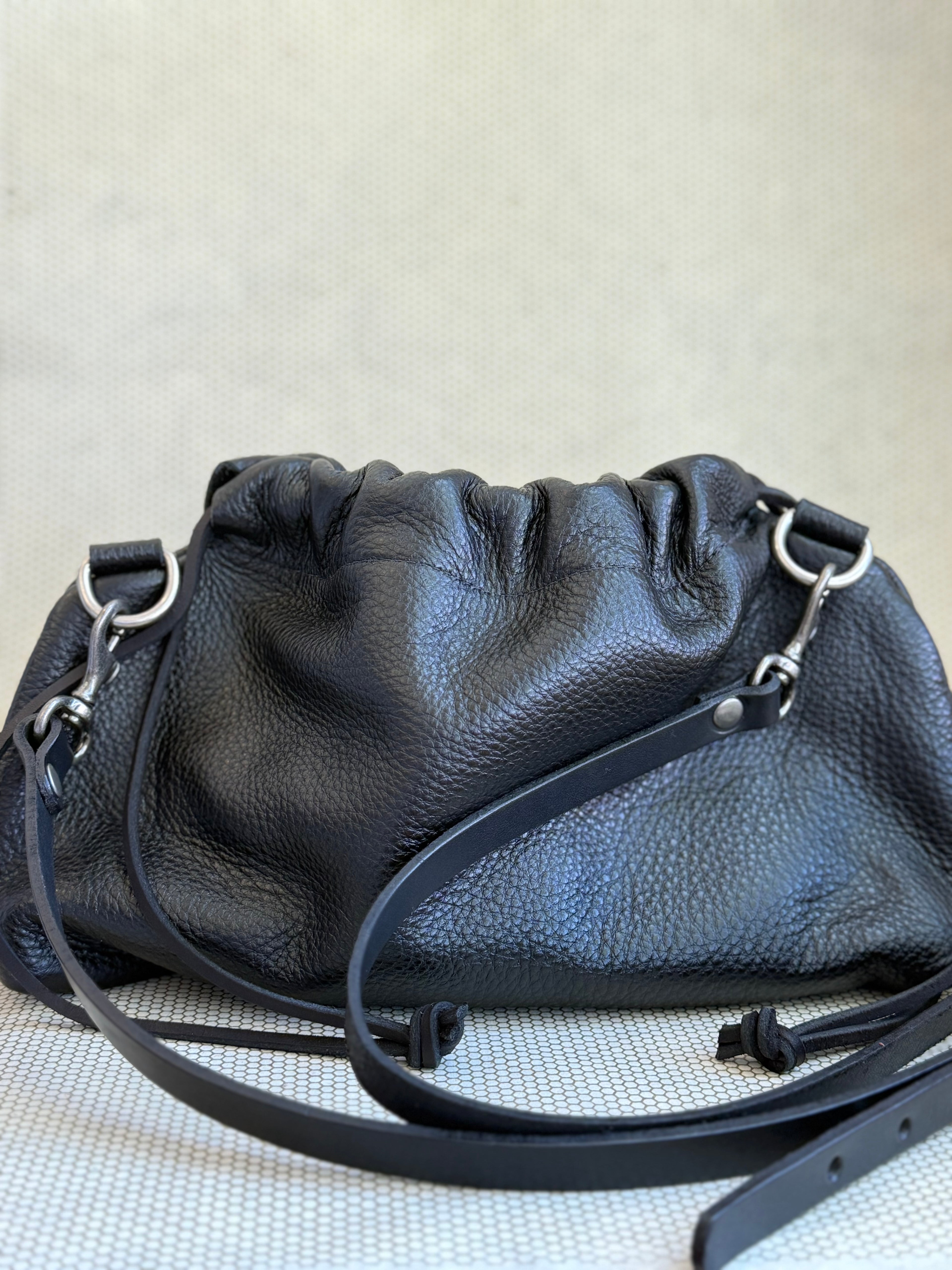 Black leather pouch bag with drawstring and strap on a light gray background.