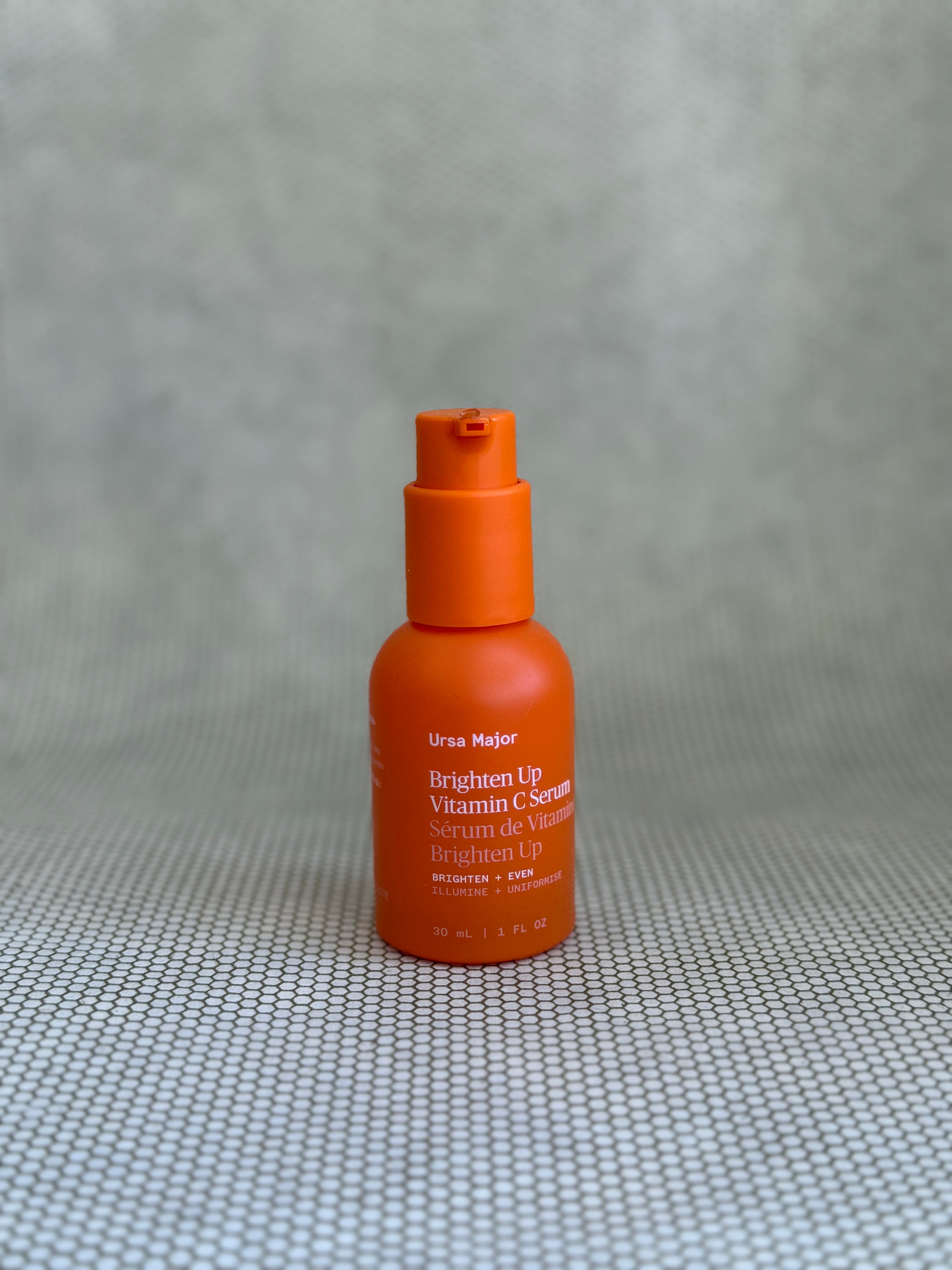 orange pump bottle of Ursa Major Brighten Up Vitamin C Serum on neutral background. 