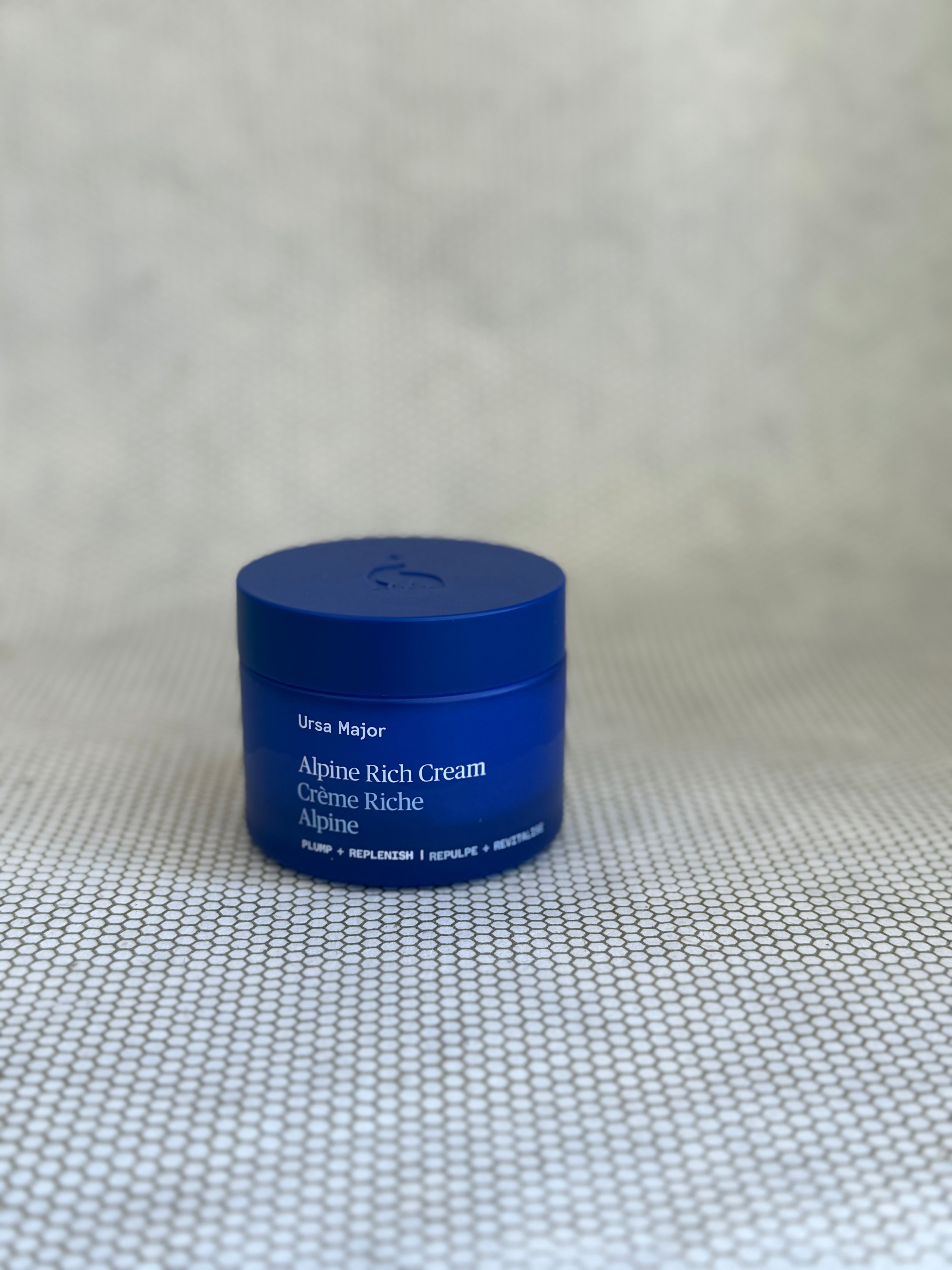 Blue jar of Ursa Major Alpine Rich Cream on a textured neutral background.