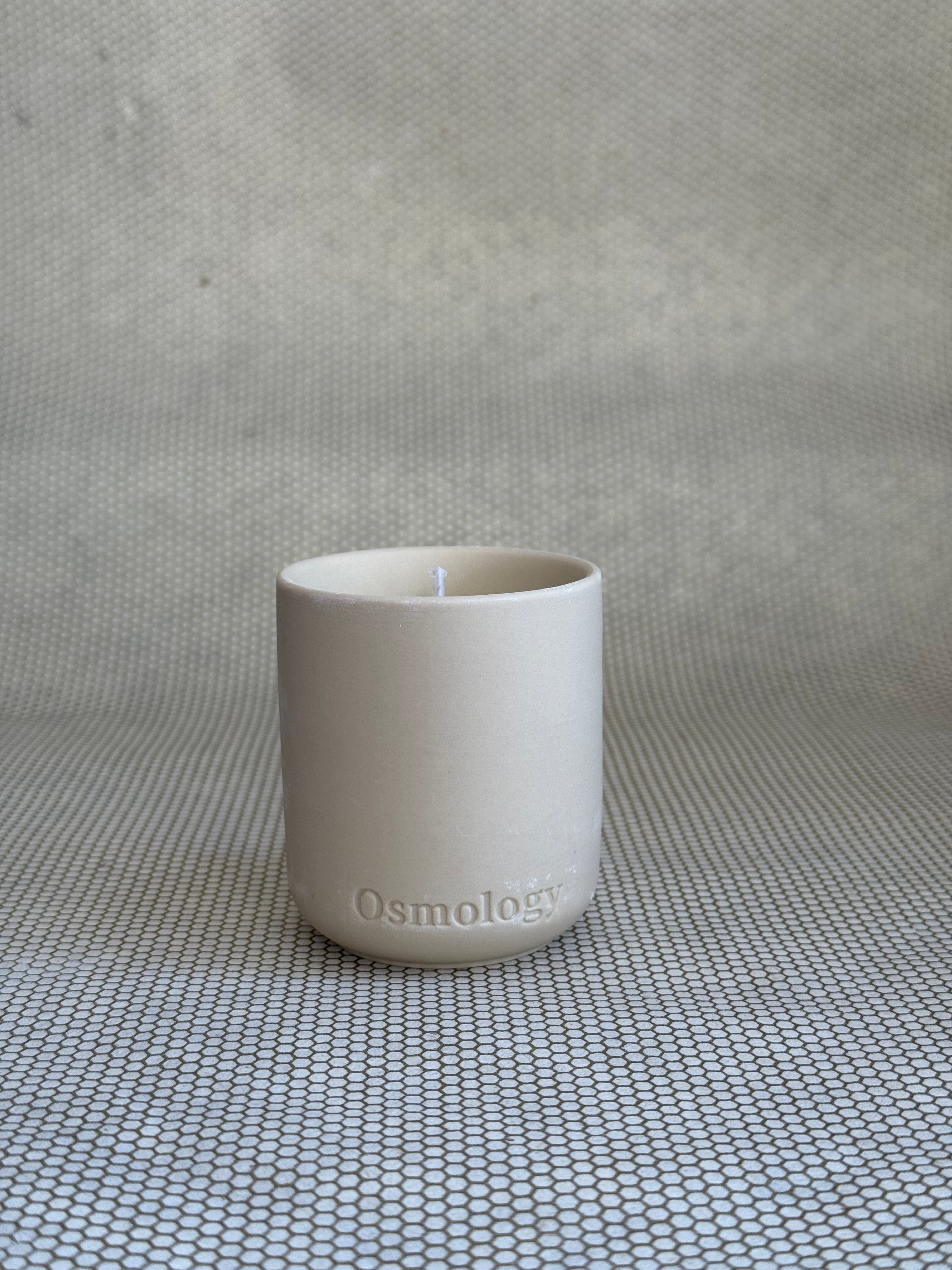 cosmology himalayan cedarleaf votive candle in neutral ceramic container on neutral background. 