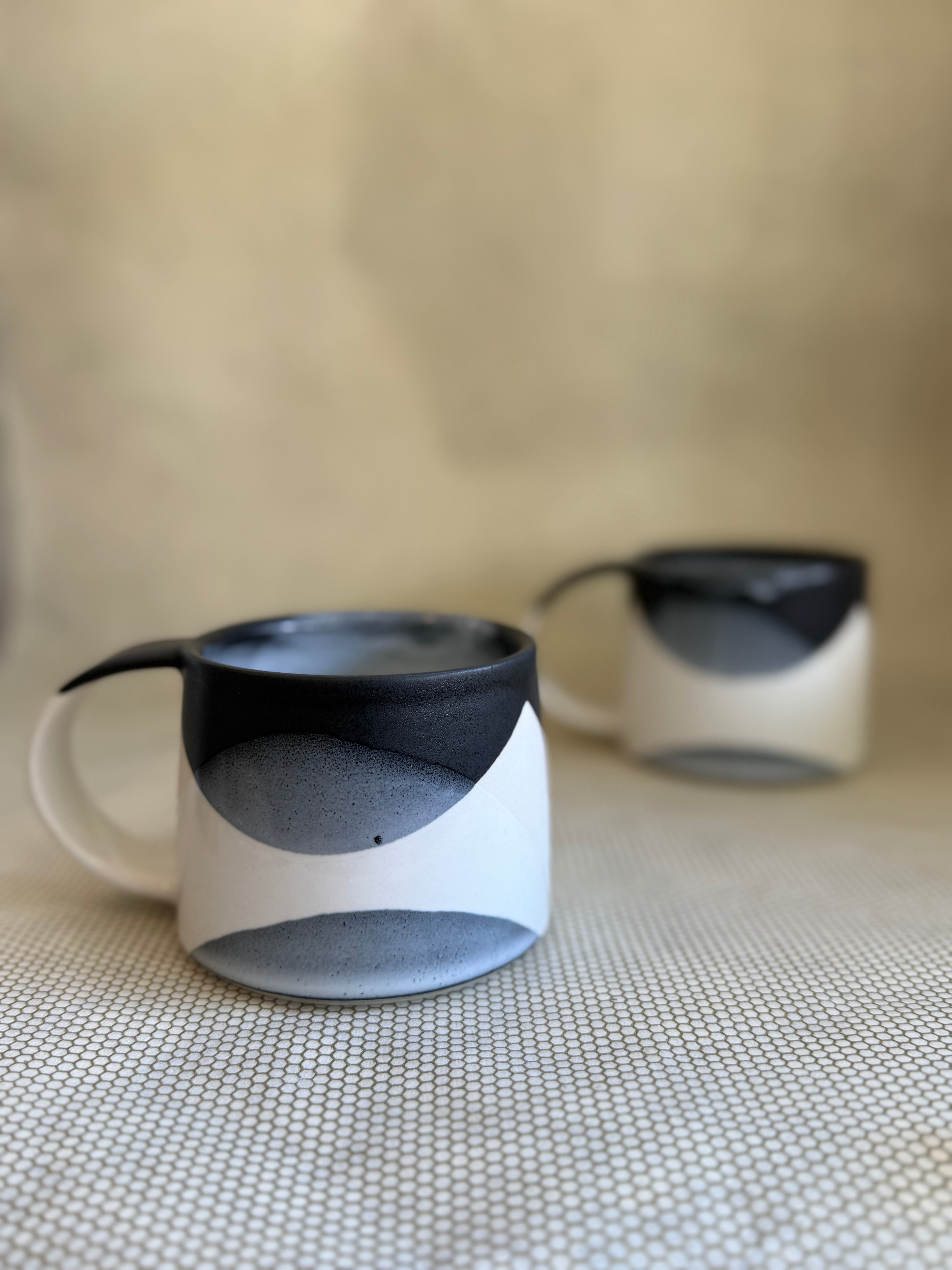 Two handcrafted ceramic mugs with black and white design on a textured surface