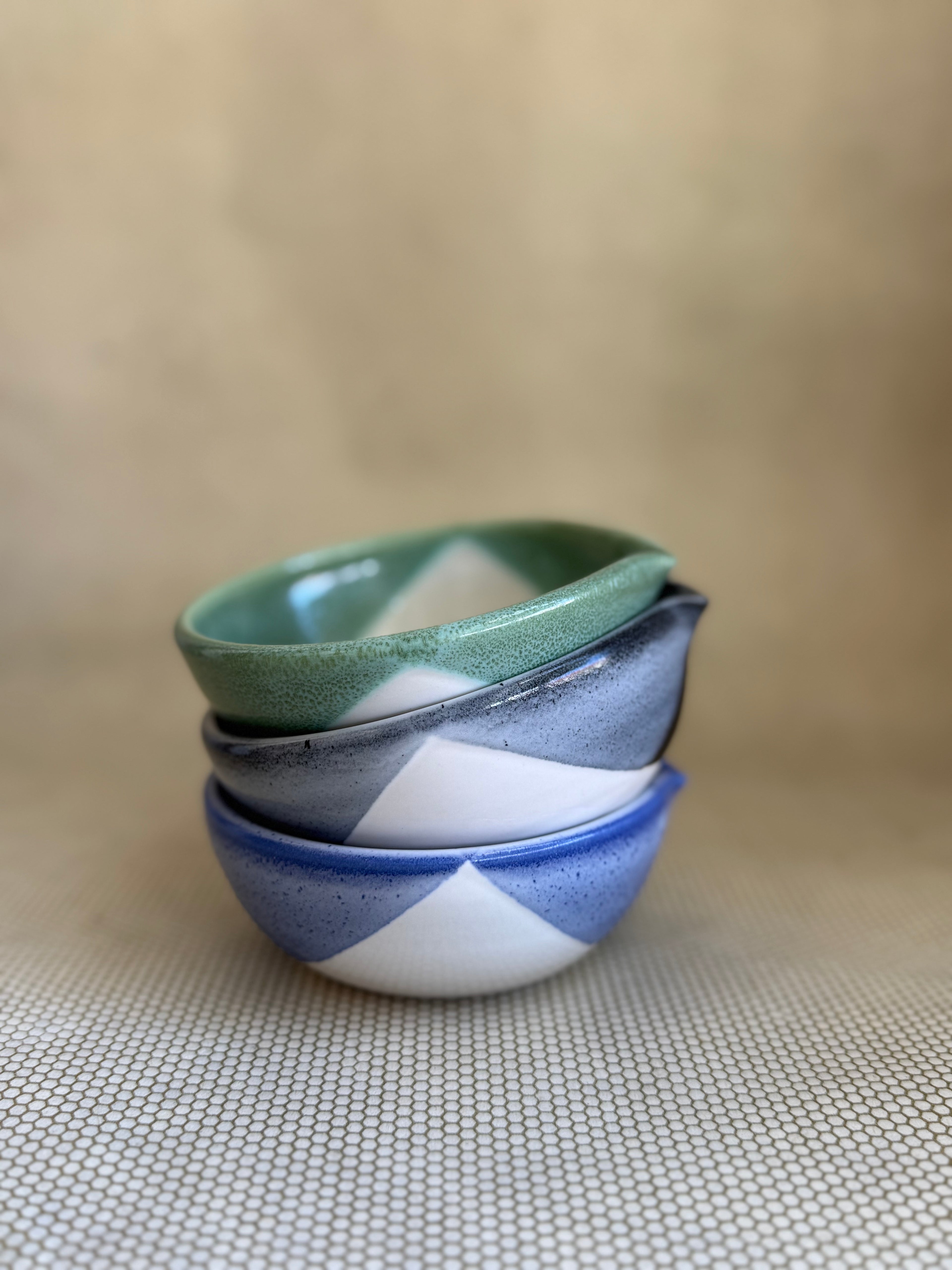 Stack of three ceramic garlic grater dishes with green, blue, and black patterns on a beige surface.