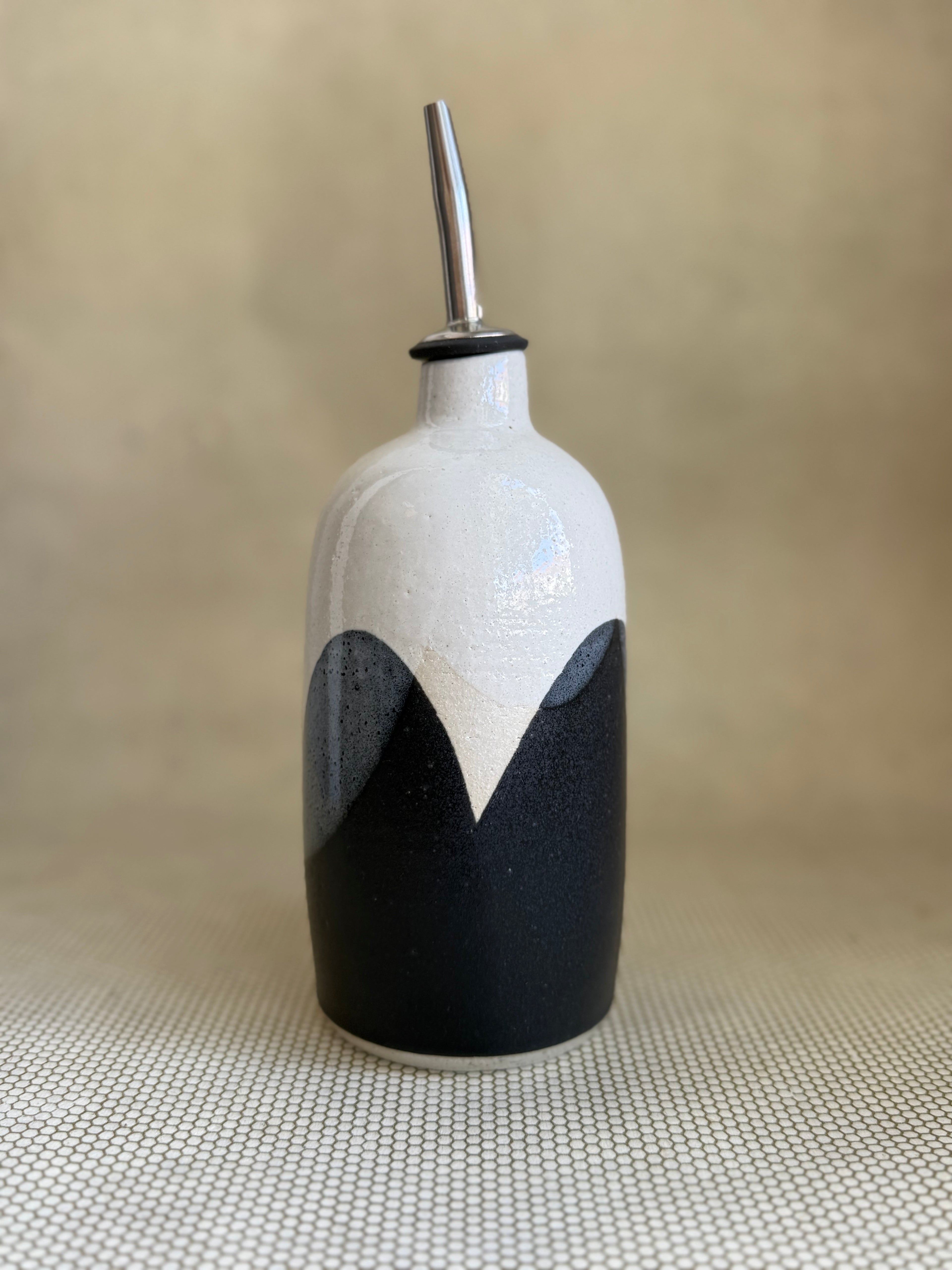 Ceramic oil cruet with black and white design on a beige background