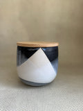 Ceramic jar with black and white geometric design and wooden lid on a textured surface