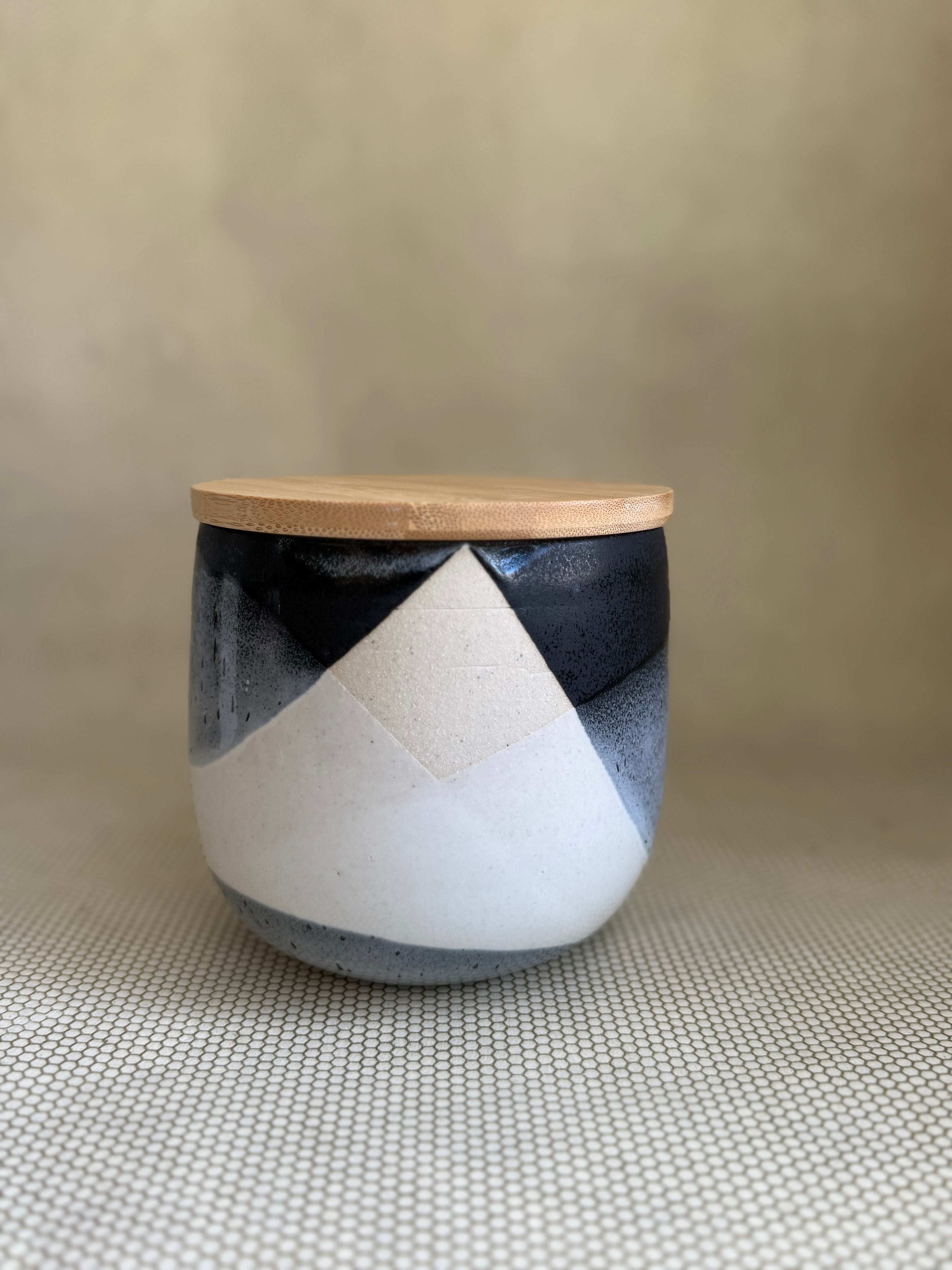 Ceramic jar with black and white geometric design and wooden lid on a textured surface
