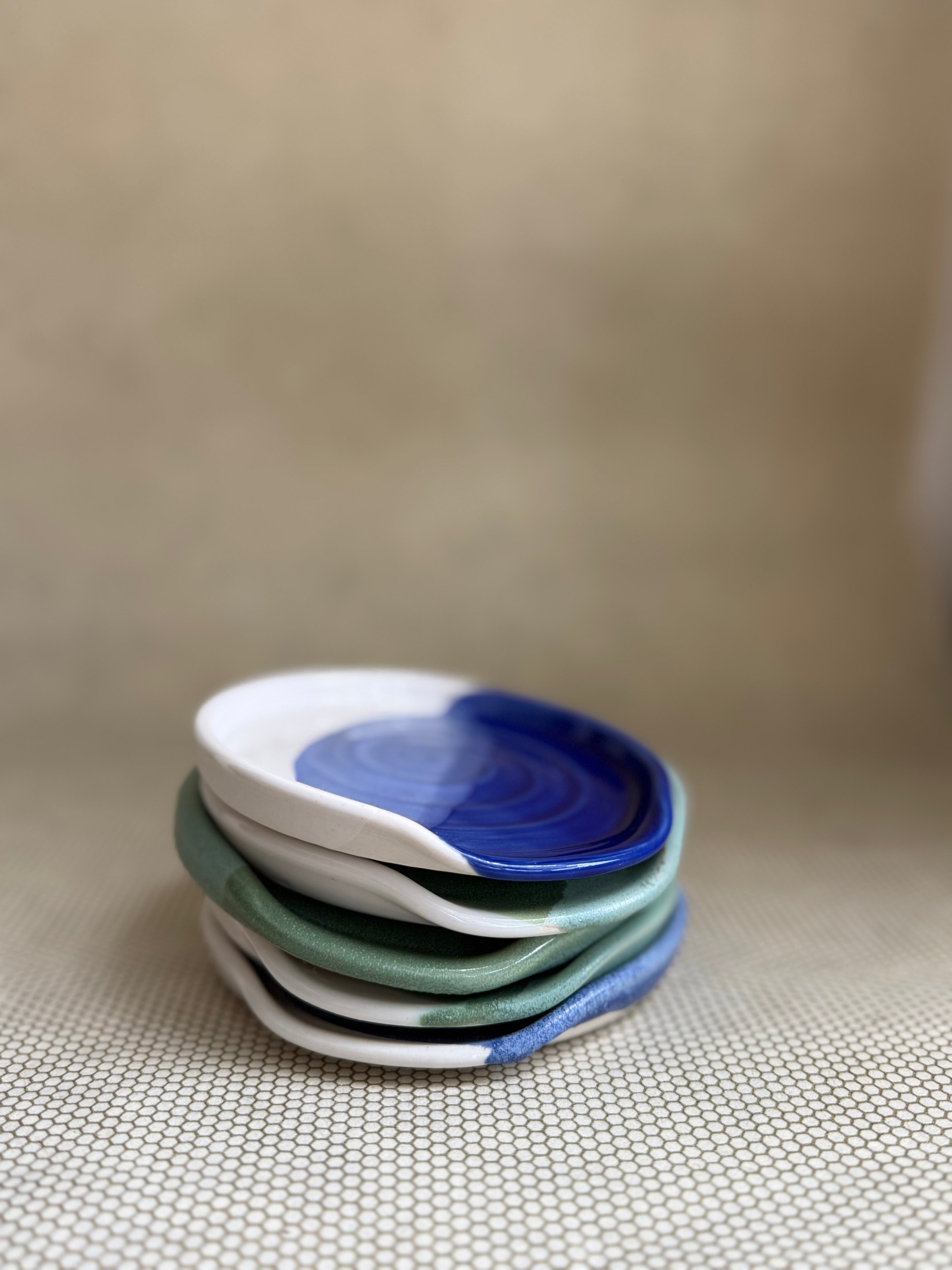 Stack of ceramic spoon rests with blue and green patterns on a neutral textured surface.