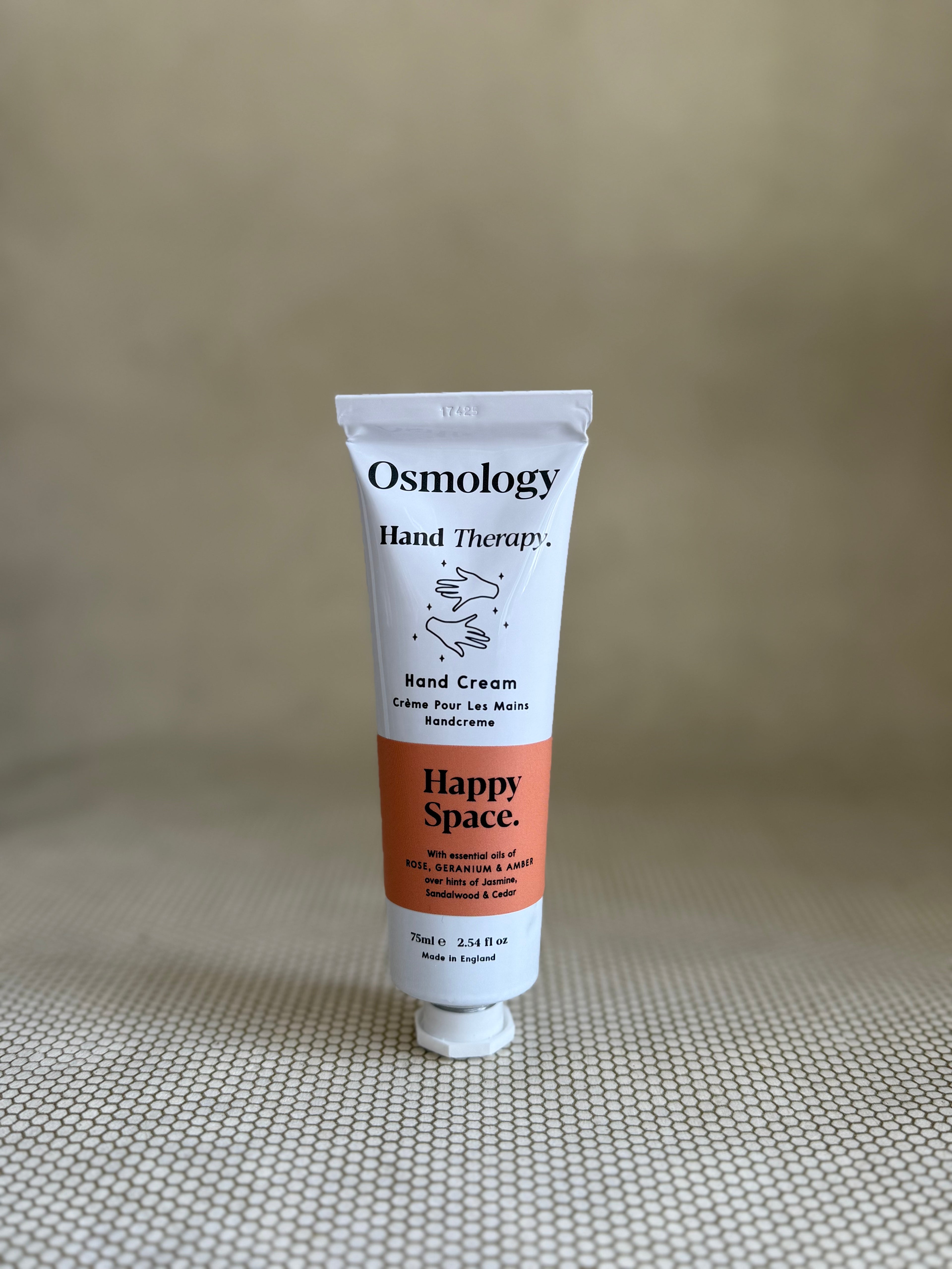 Osmology Hand Therapy Happy Space Hand Cream tube on a textured beige background