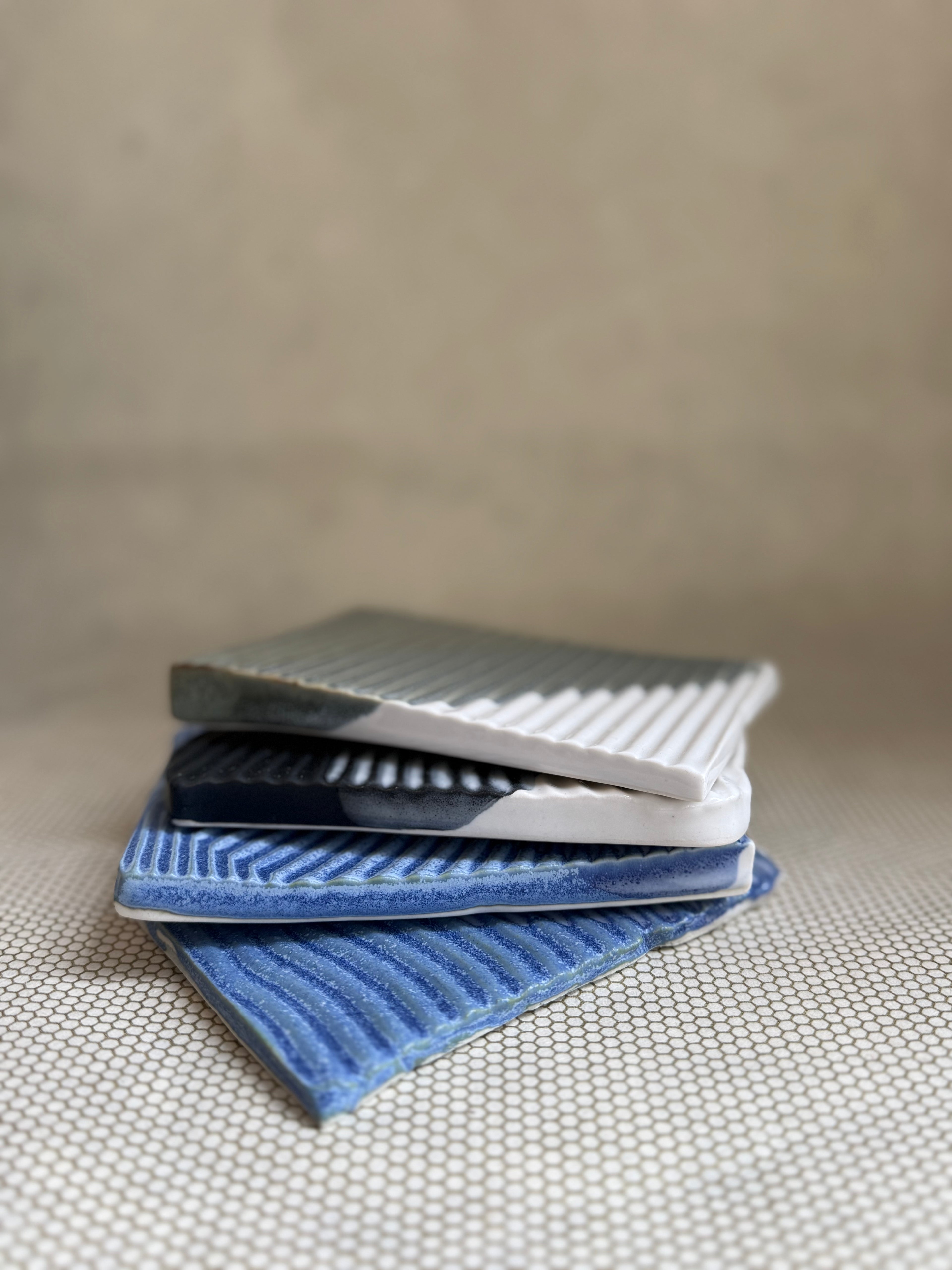 Stack of textured ceramic soap dishes in green, black, and blue designs on a neutral background.