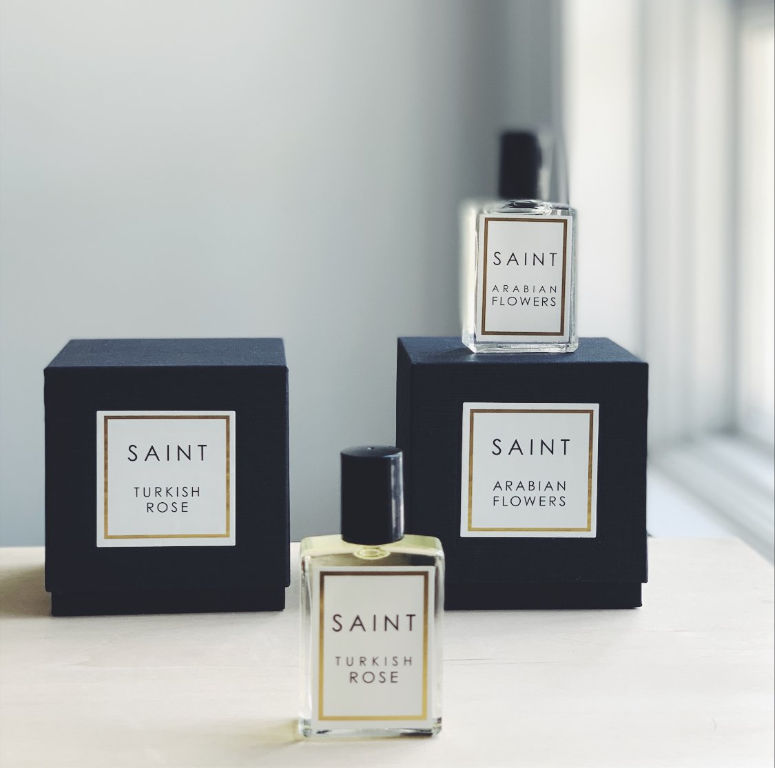 glass SAINT roll-on perfume bottles with black packaging boxes on white background. 