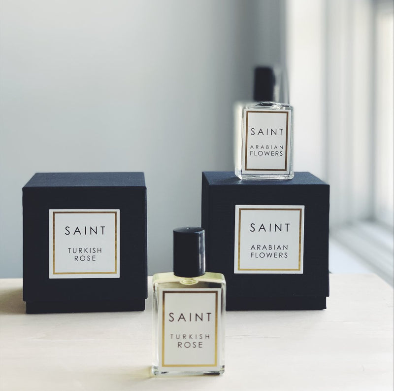 glass SAINT roll-on perfume bottles with black packaging boxes on white background. 